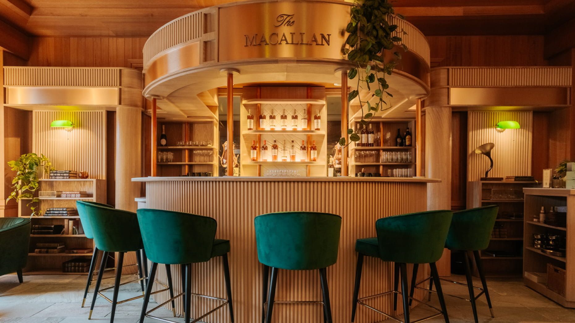 Bar with a wooden facade, The Macallan sign, green velvet stools, and lush plants.
