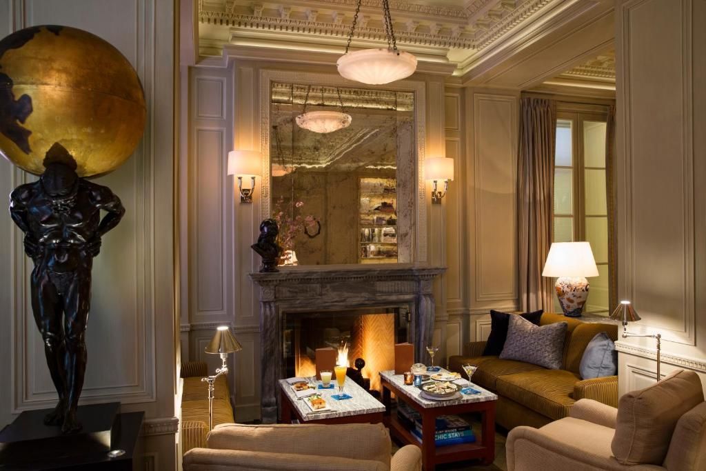 The Lowell – Upper East Side Luxurious living room with fireplace, statue of Atlas, couches, and a large mirror. Warm lighting and decorative ceiling.
