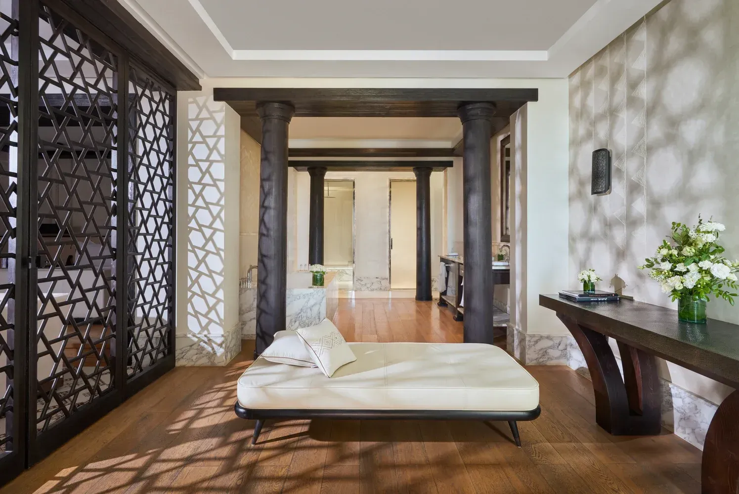 Elegant room with daybed, dark columns, decorative screen, wooden table with flowers and a hallway in the background. The Mandarin Oriental, Marrakech