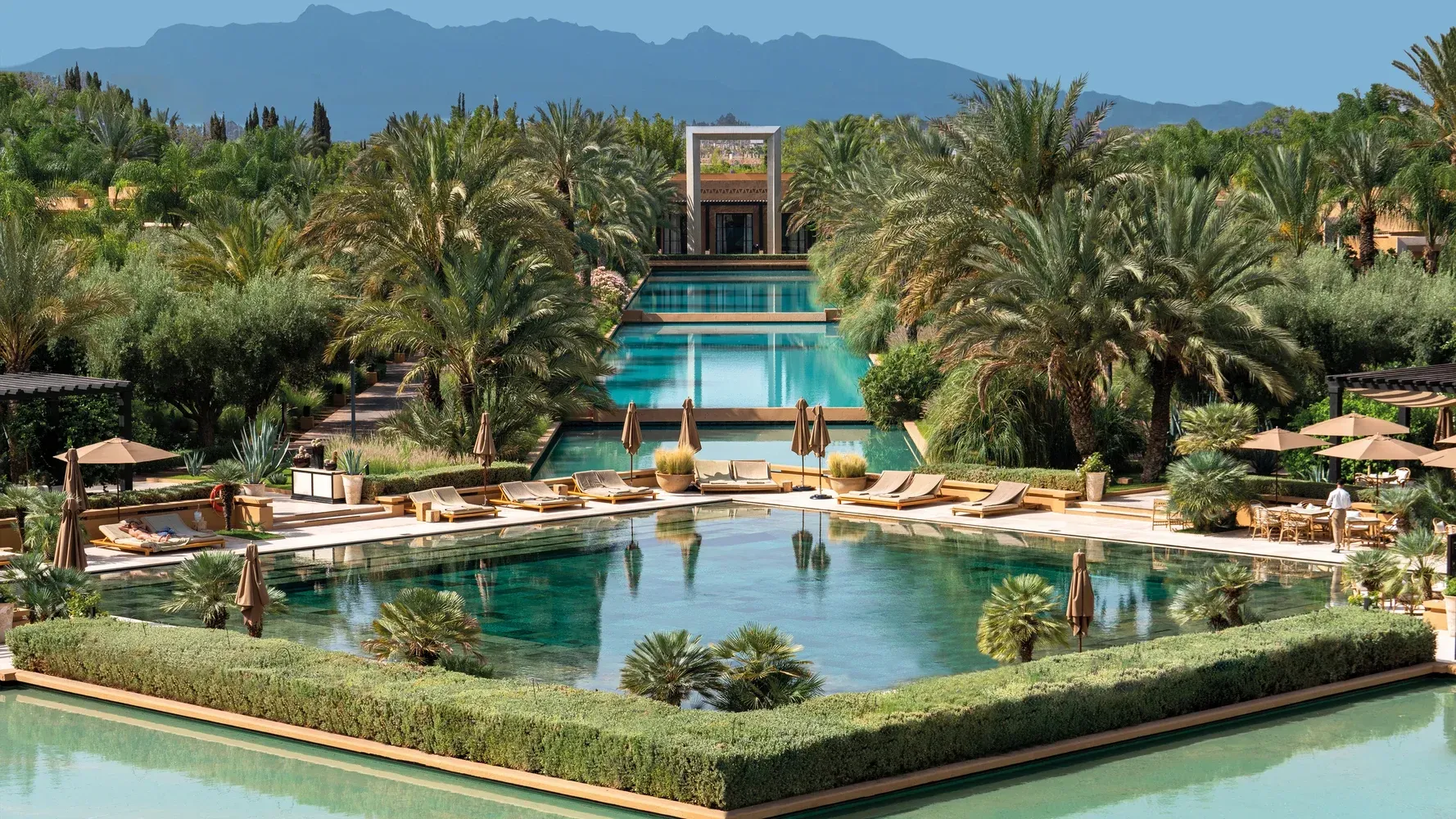 Luxury resort pools surrounded by palm trees, mountains in the distance. The Mandarin Oriental, Marrakech