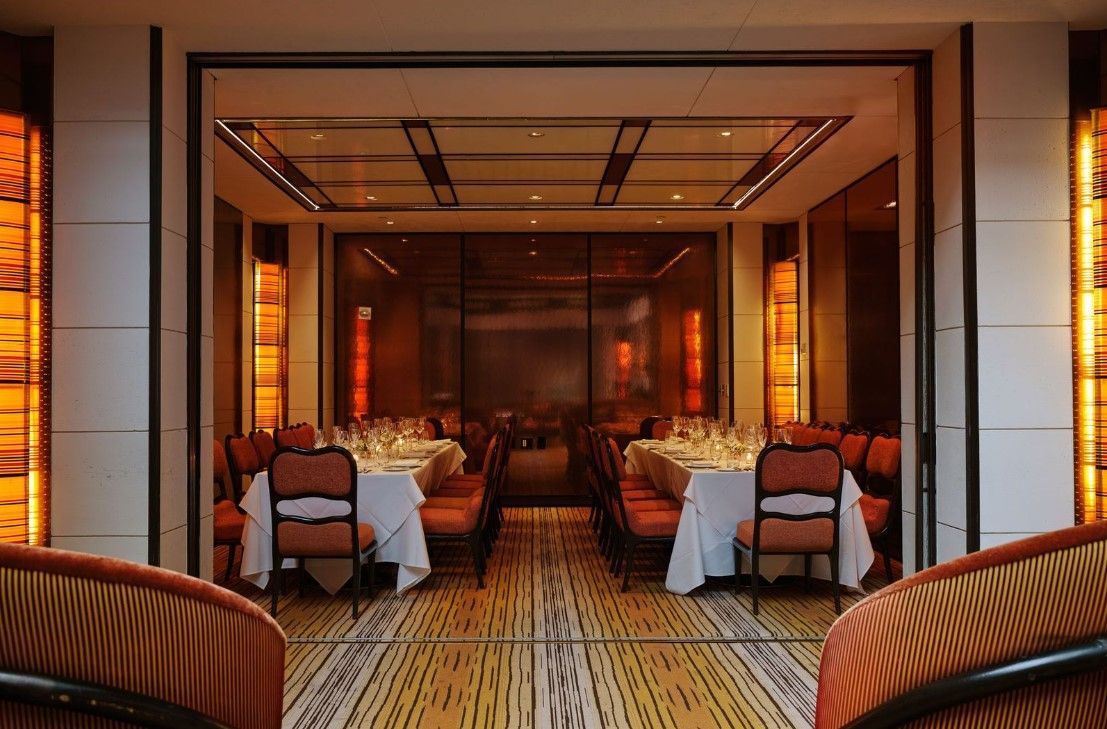 The Mark Hotel – Upper East Side Formal dining room with long tables set for a meal. The room has orange accents, white tablecloths, and a patterned floor.