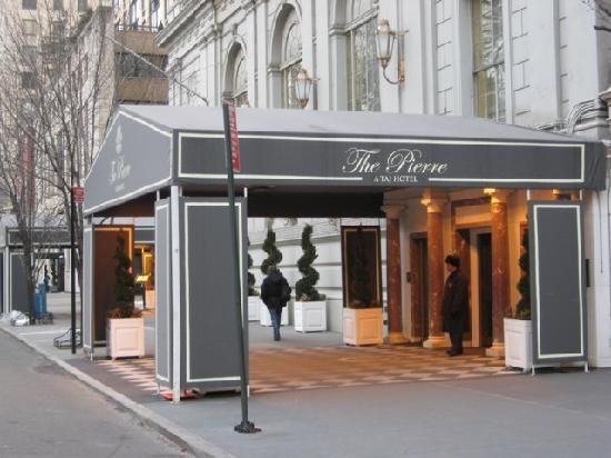 The Pierre – Fifth Avenue & Central Park Entrance to The Pierre, A Taj Hotel, NYC. Gray awning over entry; people enter and exit.