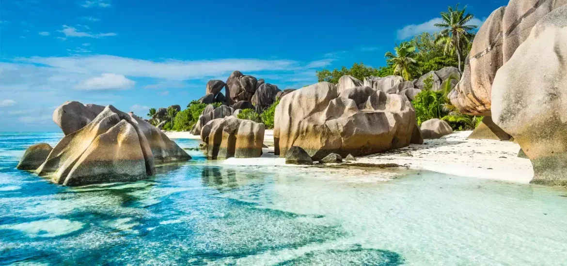 Idyllic beach scene: large granite boulders on a white sand beach with turquoise water under a clear blue sky.