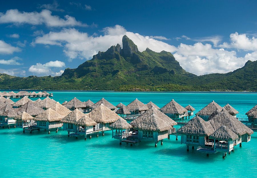 The St. Regis Bora Bora Resort Overwater bungalows in turquoise water with a lush green mountain backdrop under a blue sky.
