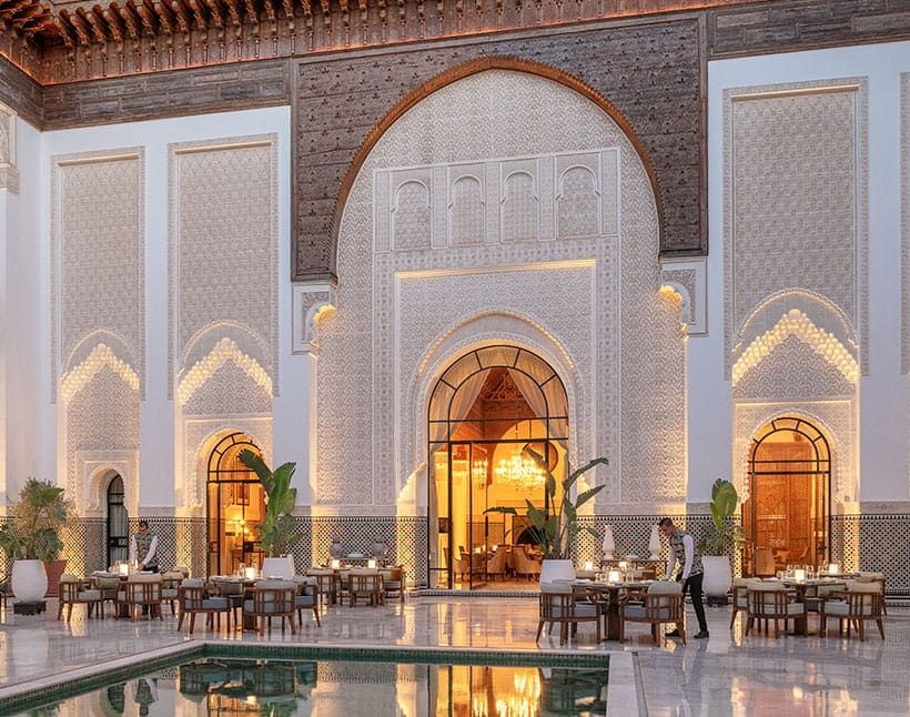 Elegant courtyard with ornate arches, warm lighting, dining tables, and a reflective pool at dusk The Oberoi, Marrakech
