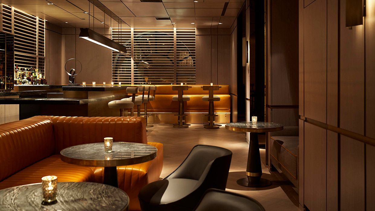 Stylish bar interior with leather seating, circular tables, and a backlit bar counter.  The Peninsula hotel on 5th Avenue, NYC