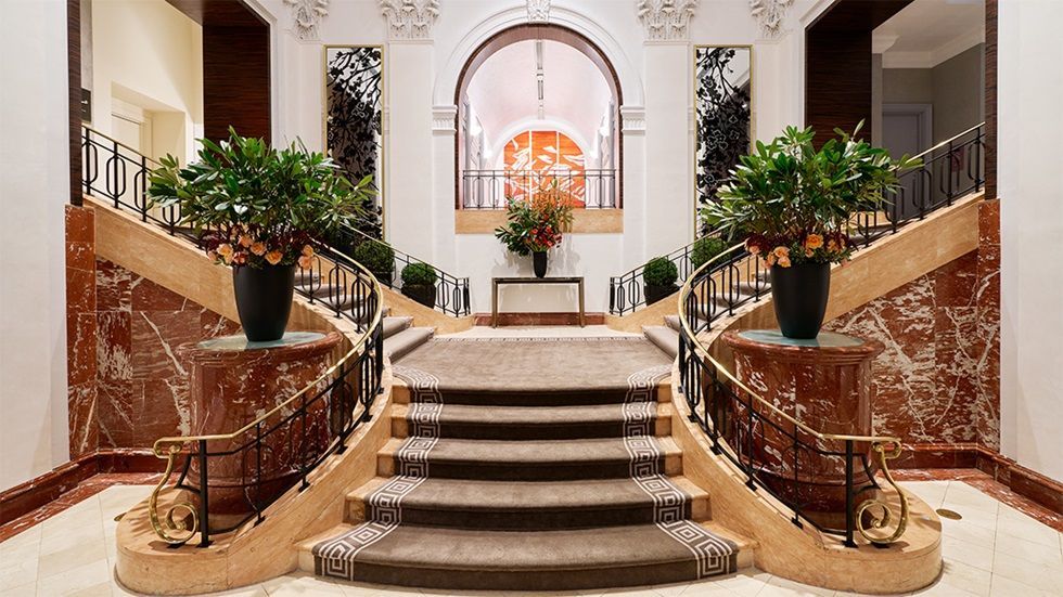 Grand staircase with marble walls, ornate railings, floral arrangements, and a central archway.  The Peninsula hotel on 5th Avenue, NYC