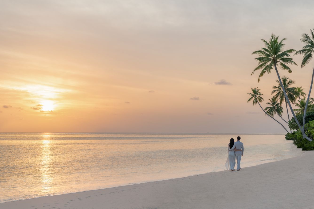 Couple watching sunset on a beach with palm trees. The St. Regis, Maldives Vommuli Resort