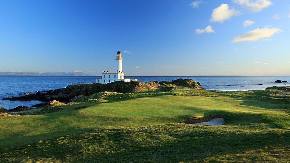 A golf course with a lighthouse on a rocky coastline under a blue sky. Trump Turnberry