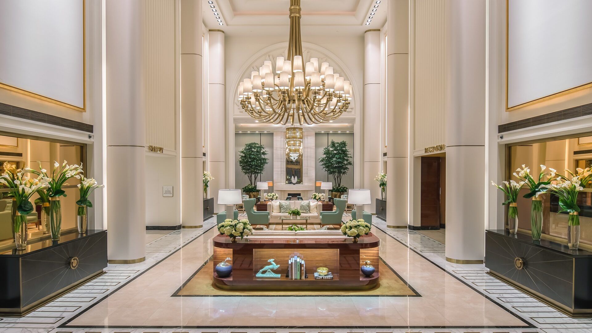 Elegant hotel lobby with marble floors, columns, large chandelier, and floral arrangements. The Waldorf Astoria, Beverly Hills: Lobby 