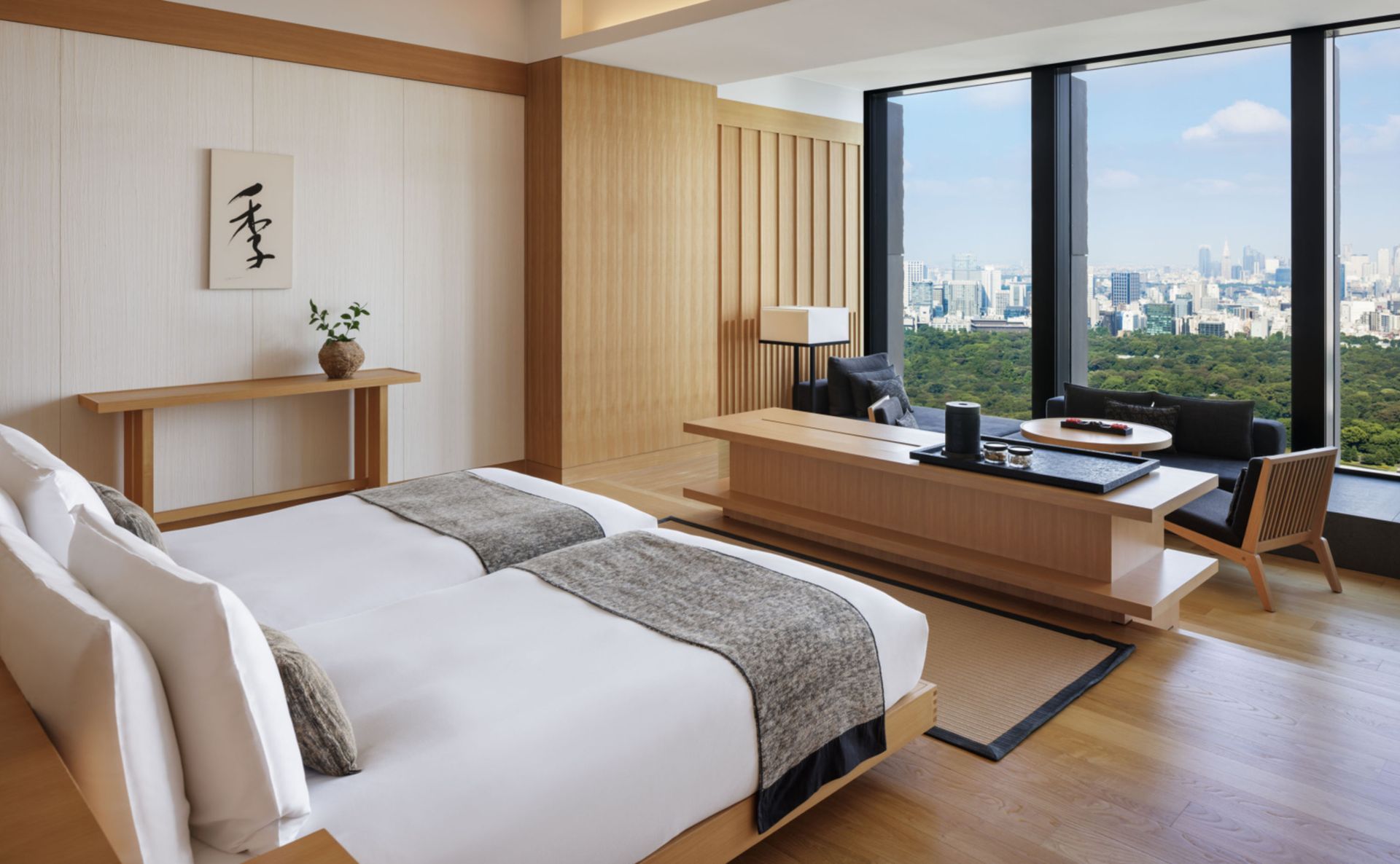 Hotel bedroom with a large window, wooden desk, and a bed with neutral-toned bedding. Aman Tokyo