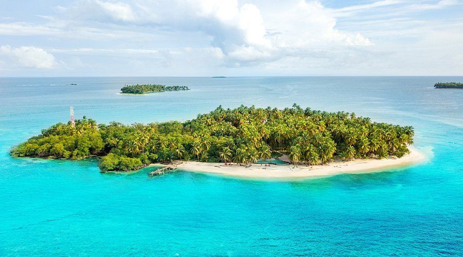 Tropical island surrounded by turquoise water, lush green vegetation, white sand beach, and small islands in the distance. Calala Island