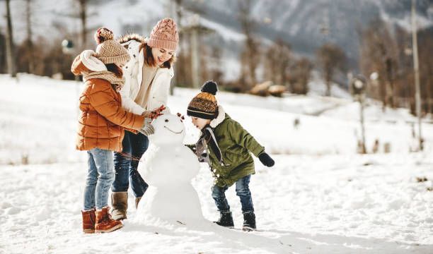 Family building a snowman in a snowy outdoor setting; the mother and children are smiling.