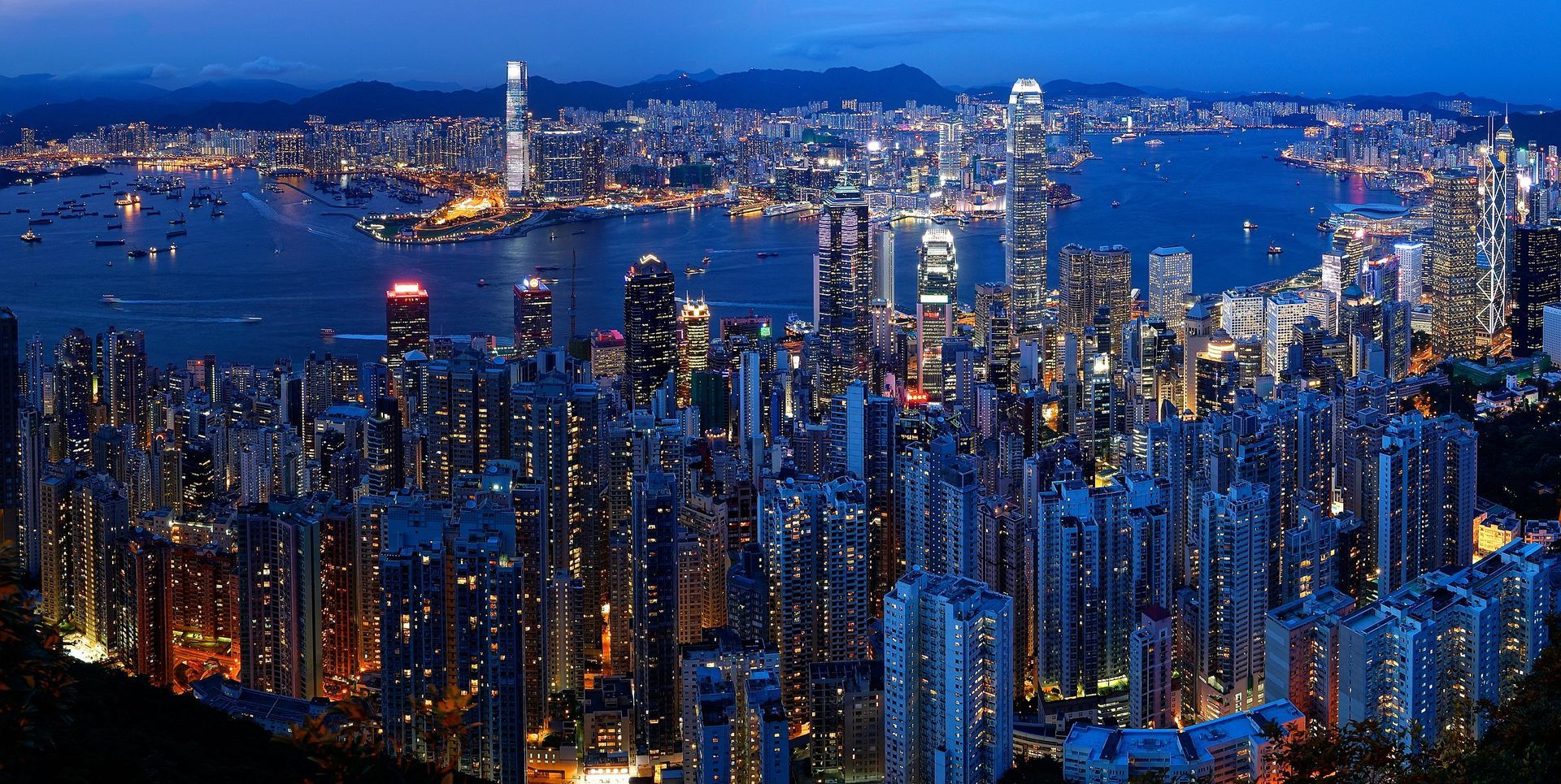 Nighttime view of a sprawling cityscape with illuminated skyscrapers along a harbor. Langham_Hotel_Hong Kong_