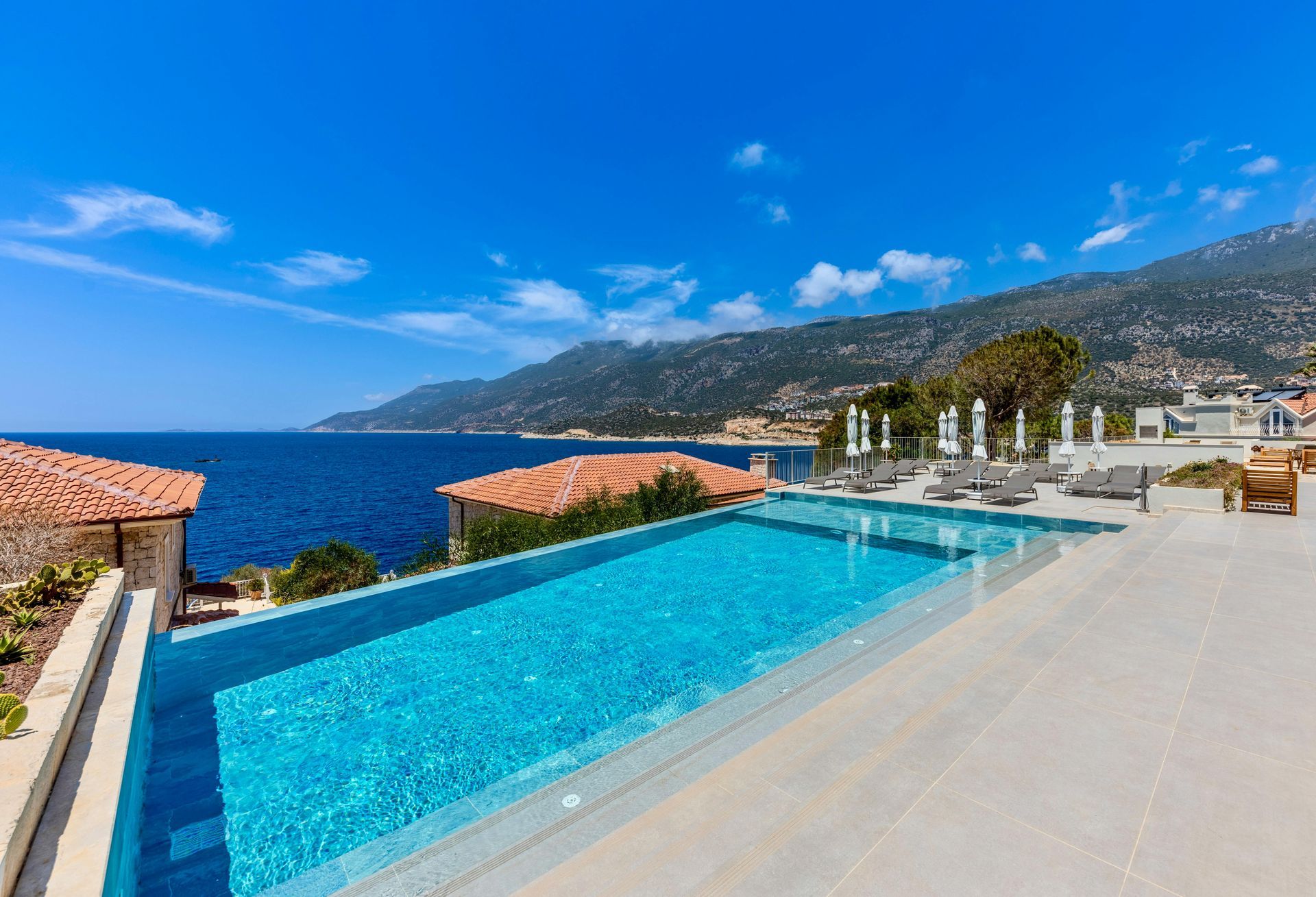 Infinity pool overlooking the ocean, mountains in the background, blue sky.