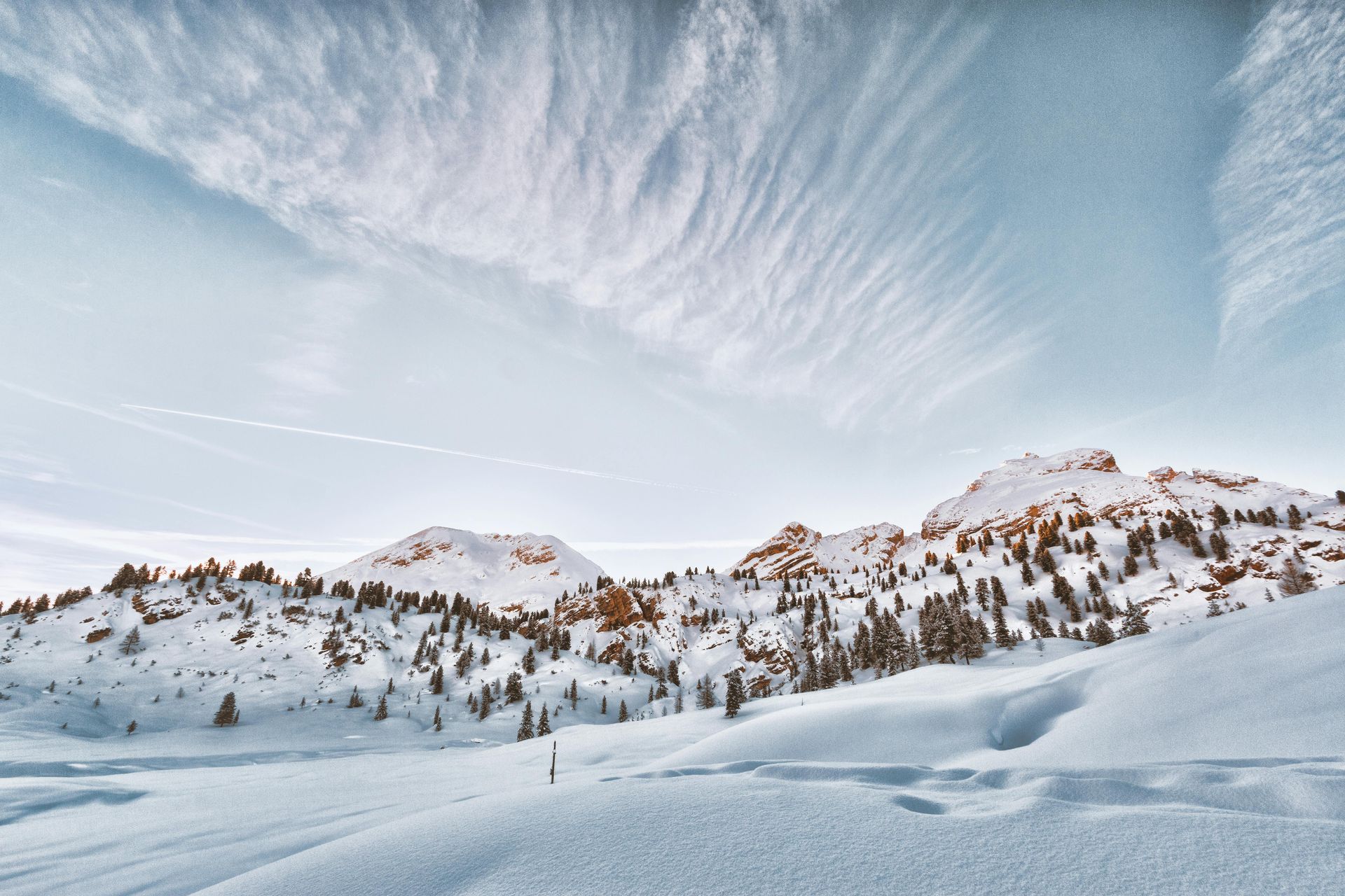 Snowy mountain landscape under a bright, cloud-filled sky. Snow covers mountains and foreground. Luxury Ski Holidays in the Dolomites