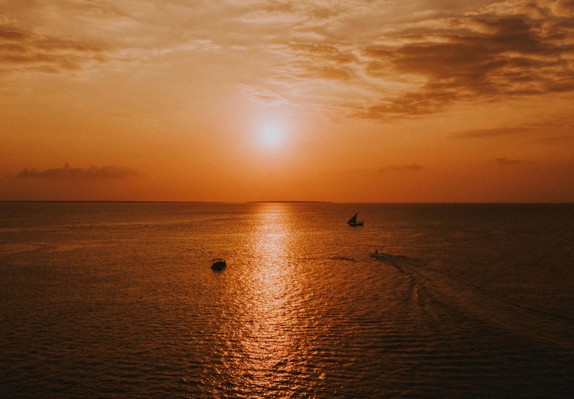 A golden sunset illuminates a calm sea with two small boats drifting in the distance.