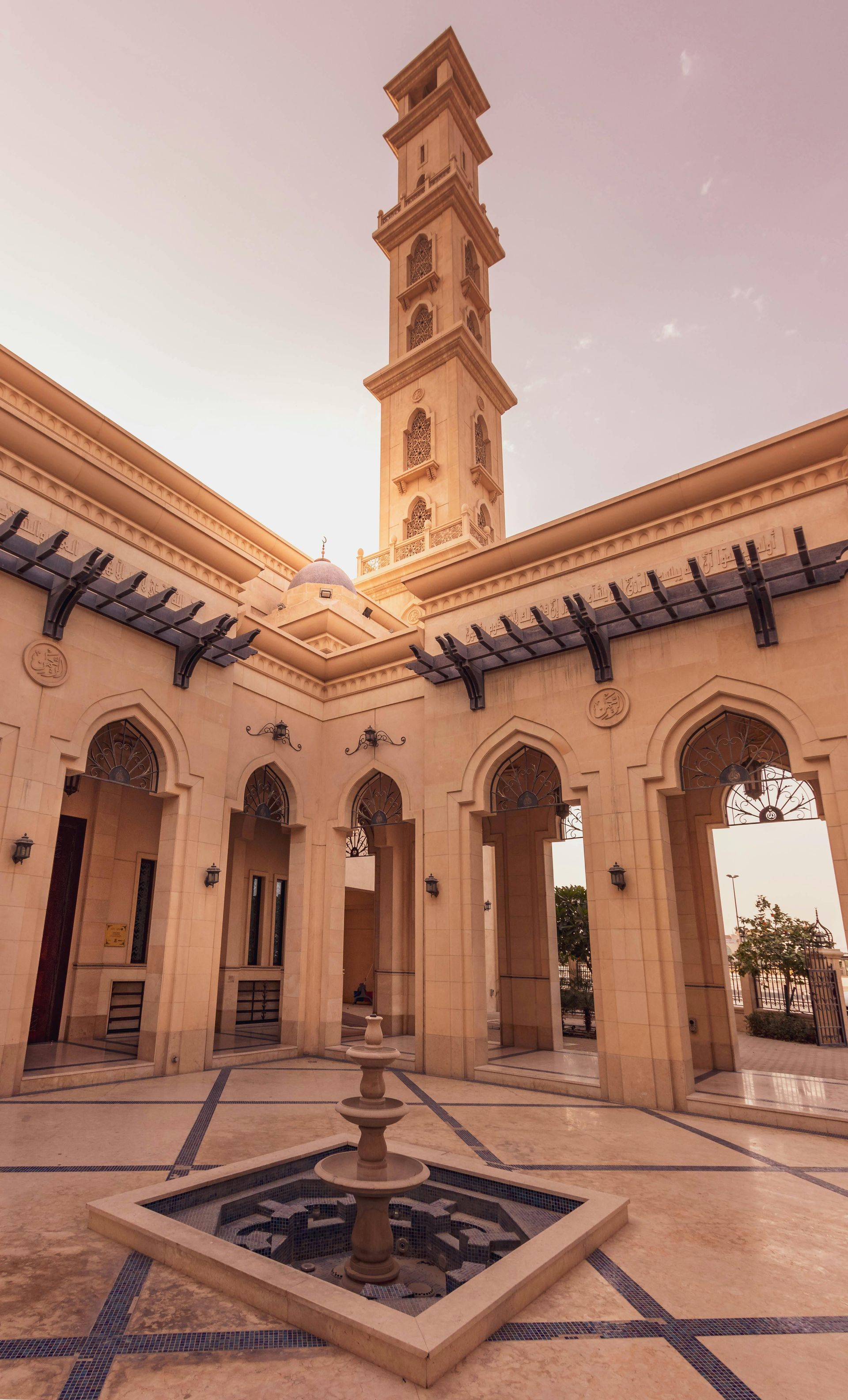 Courtyard with a fountain, arched walkways, and a tall minaret under a warm sky.