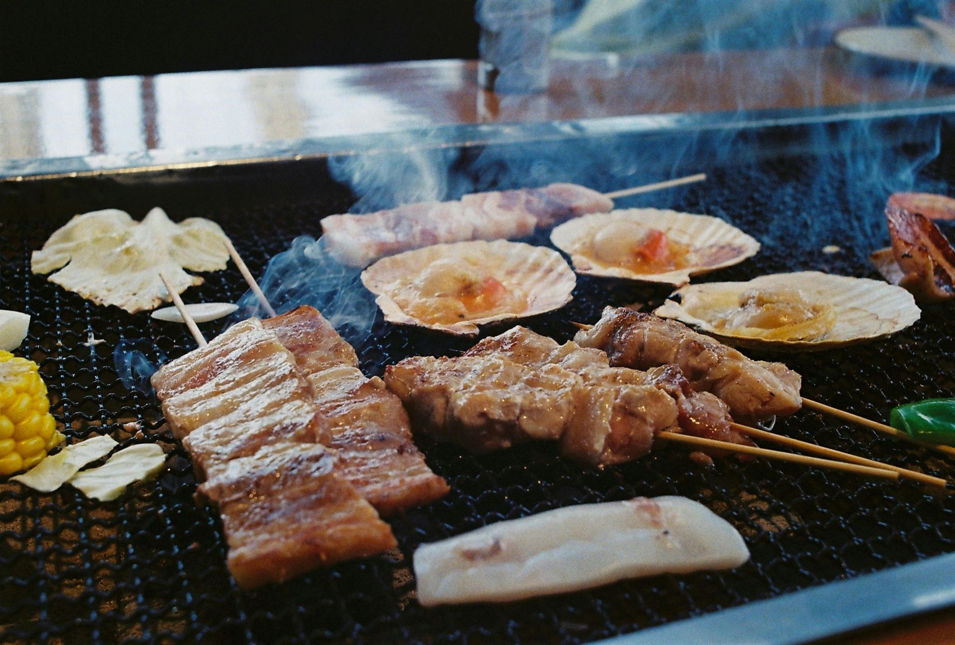 Grilled skewers and seafood on a barbecue grill, smoke rising.