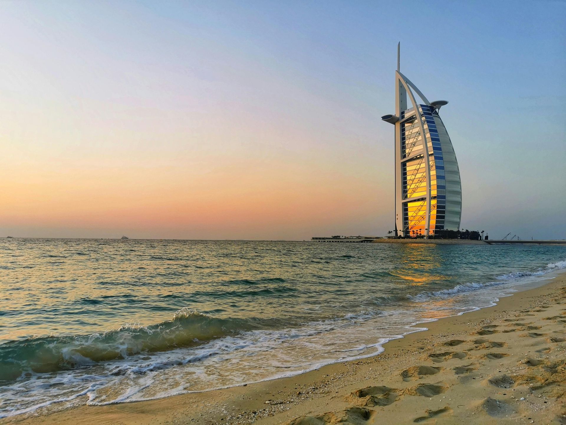 Beach view of Burj Al Arab at sunset, gold light reflecting on the sail-shaped hotel. Burj Al Arab Jumeirah