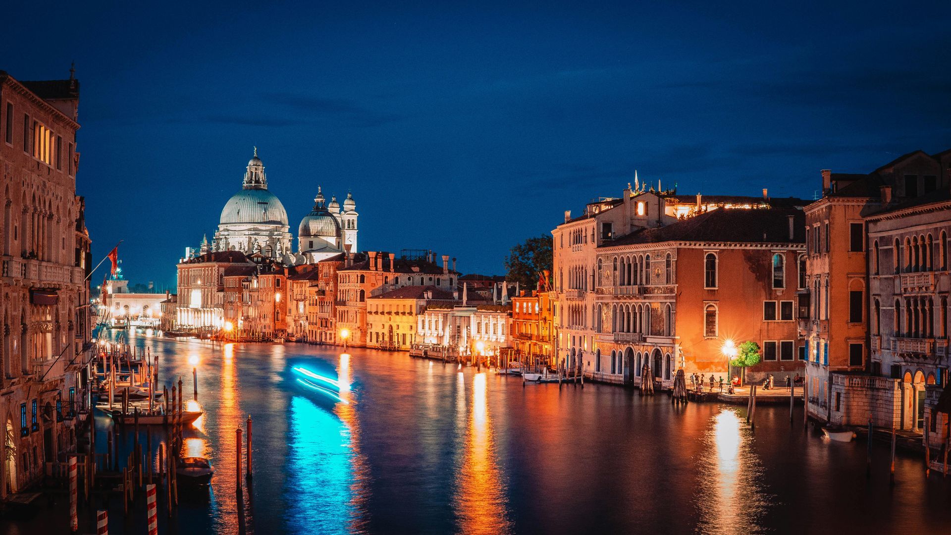 Venice canal at night with illuminated buildings reflecting in the water; Santa Maria della Salute in the background.