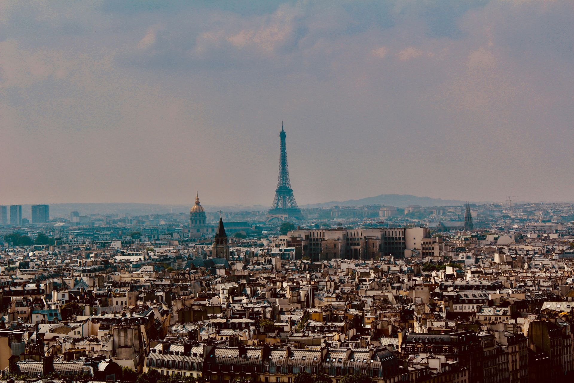 Paris cityscape with the Eiffel Tower prominent in the center, under a cloudy sky.