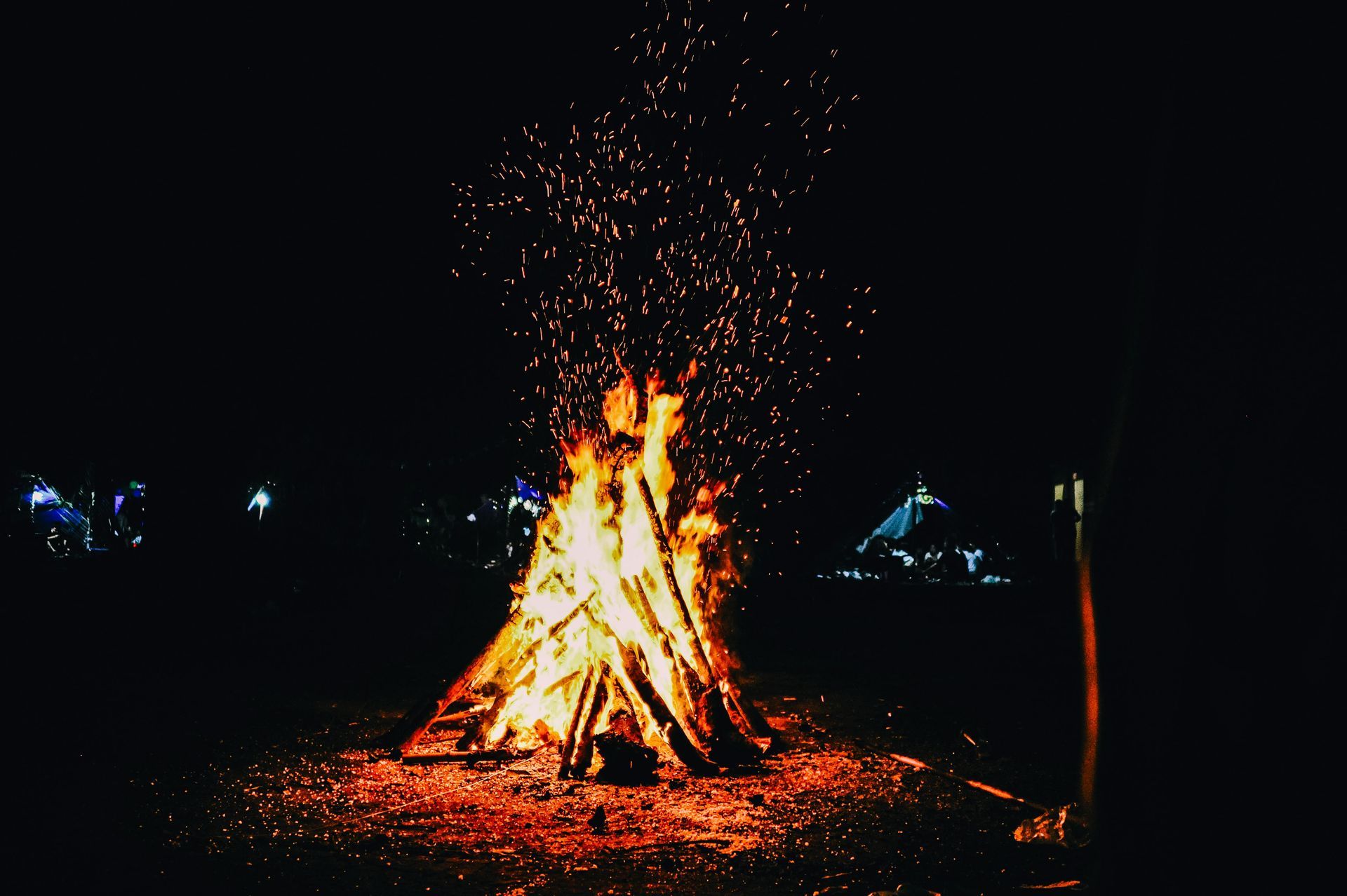 Large bonfire at night with sparks rising into the dark sky.