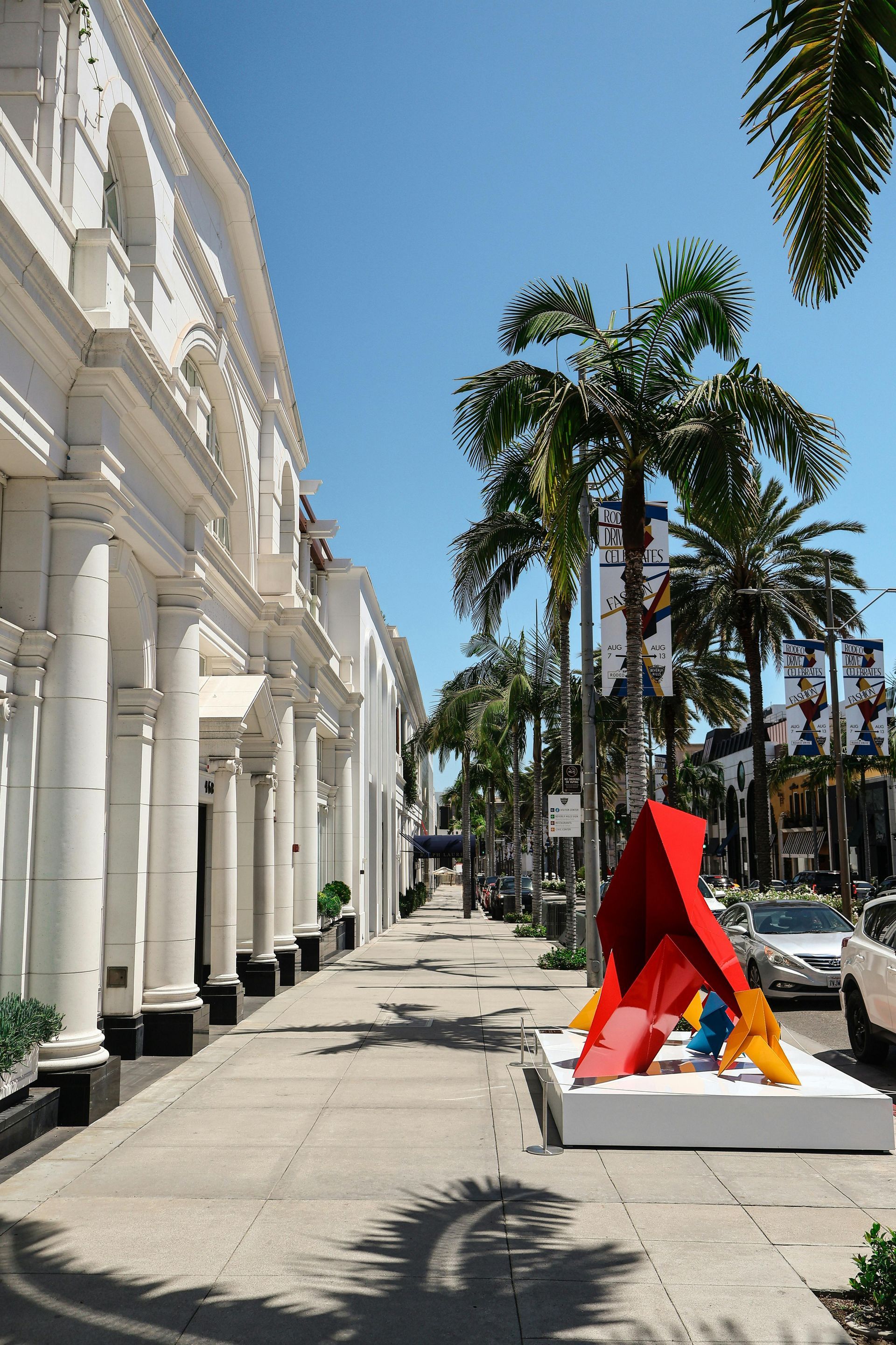 Sidewalk on Rodeo Drive, Beverly Hills, with palm trees and modern art sculpture, sunny day. Rodeo Drive