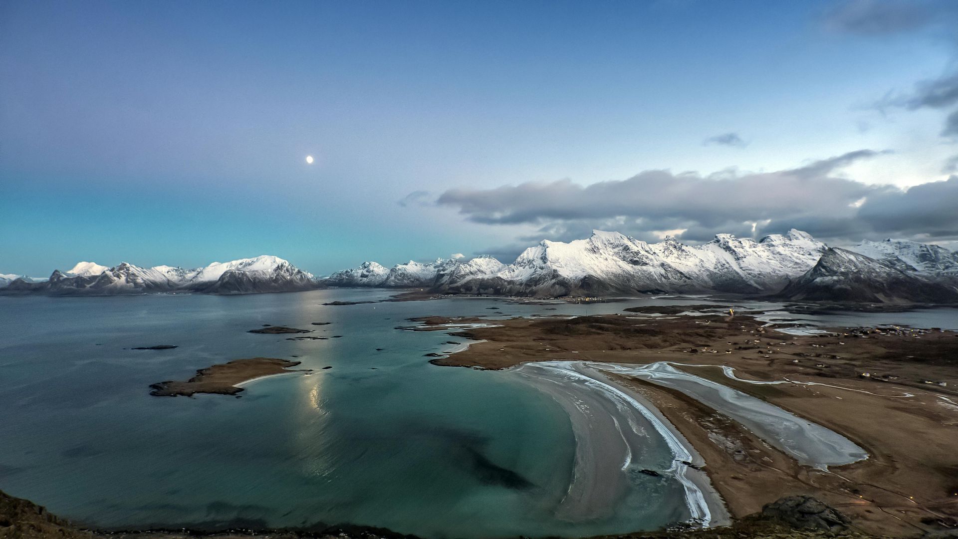 A scenic, wide-angle view of a crescent-shaped sandy beach, turquoise waters, and snow-capped mountains under a moonlit sky.