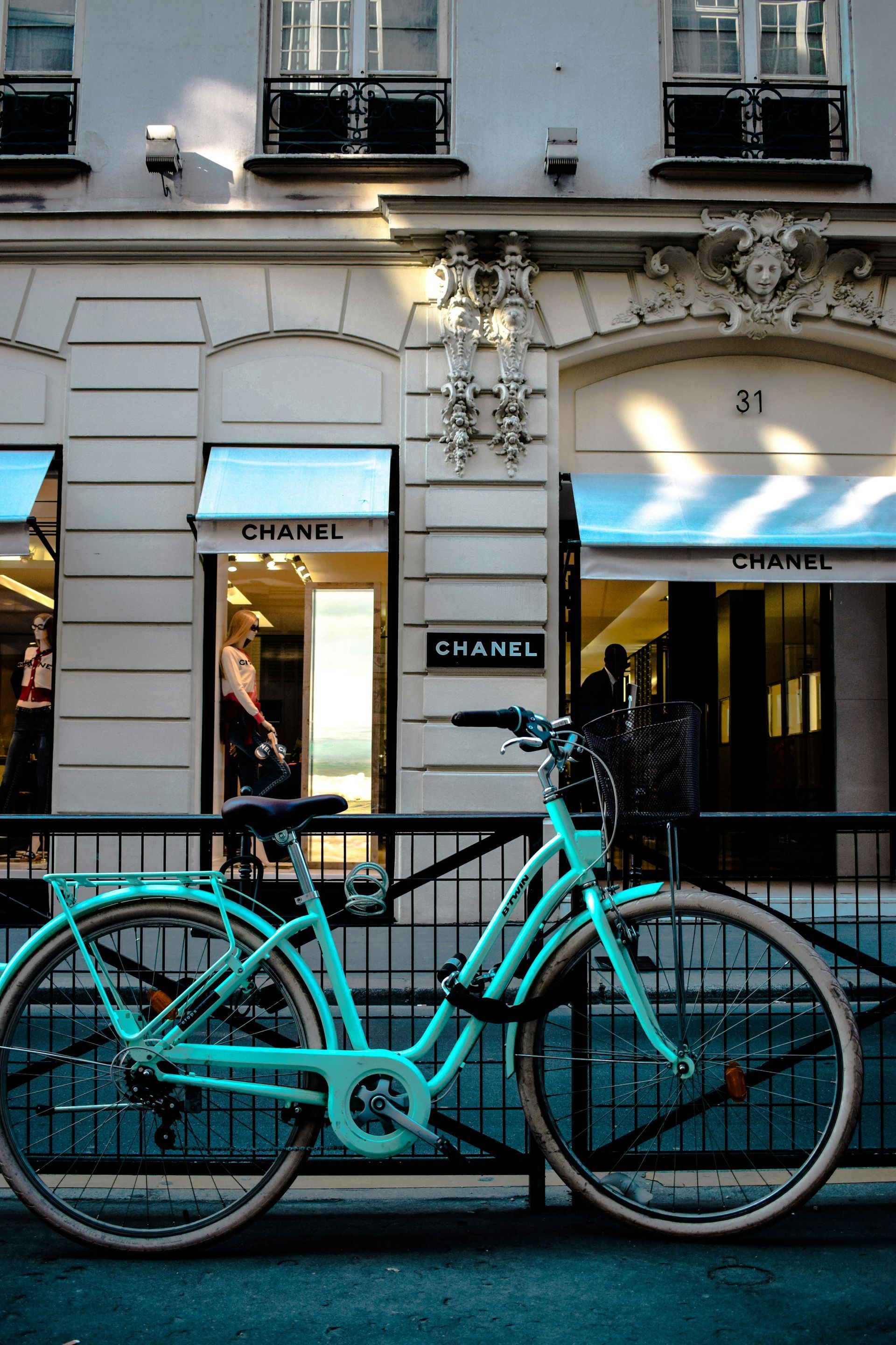 Teal bicycle parked in front of a Chanel store in a European city.