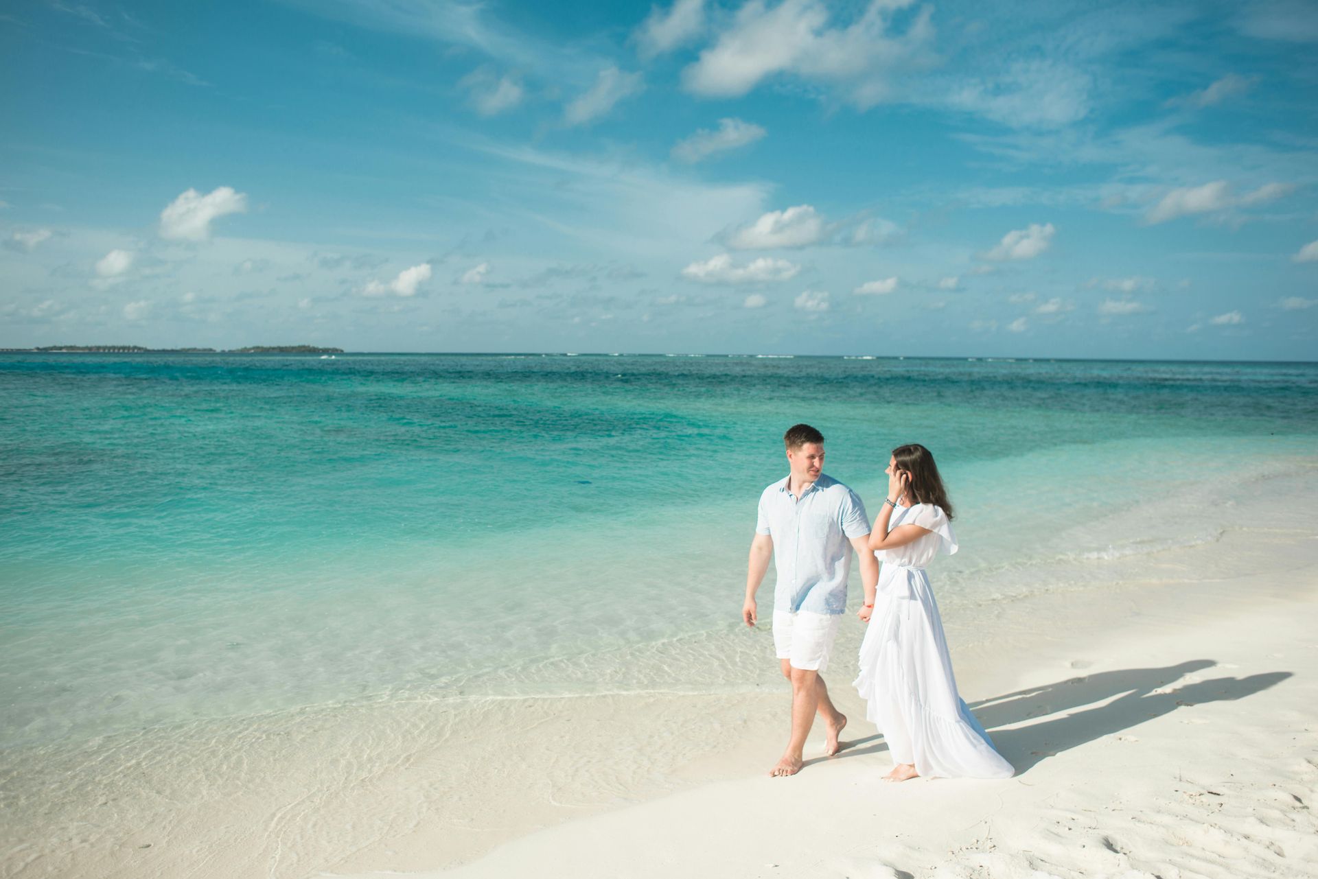 Couple walking on a white sand beach, holding hands, turquoise water, blue sky. Maldives