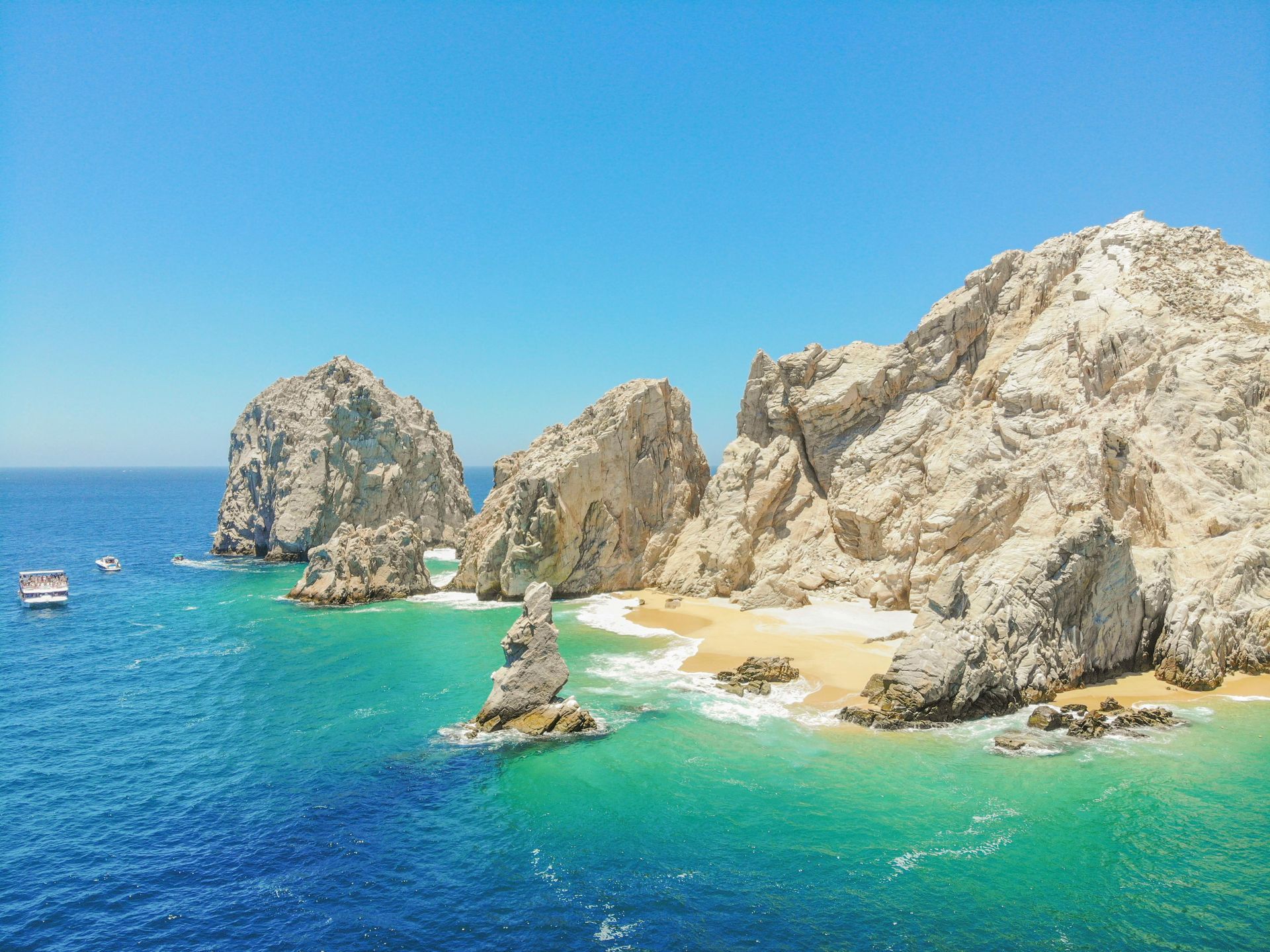 Turquoise cove with sandy beach, rocky cliffs, and a clear blue sea under bright sunlight