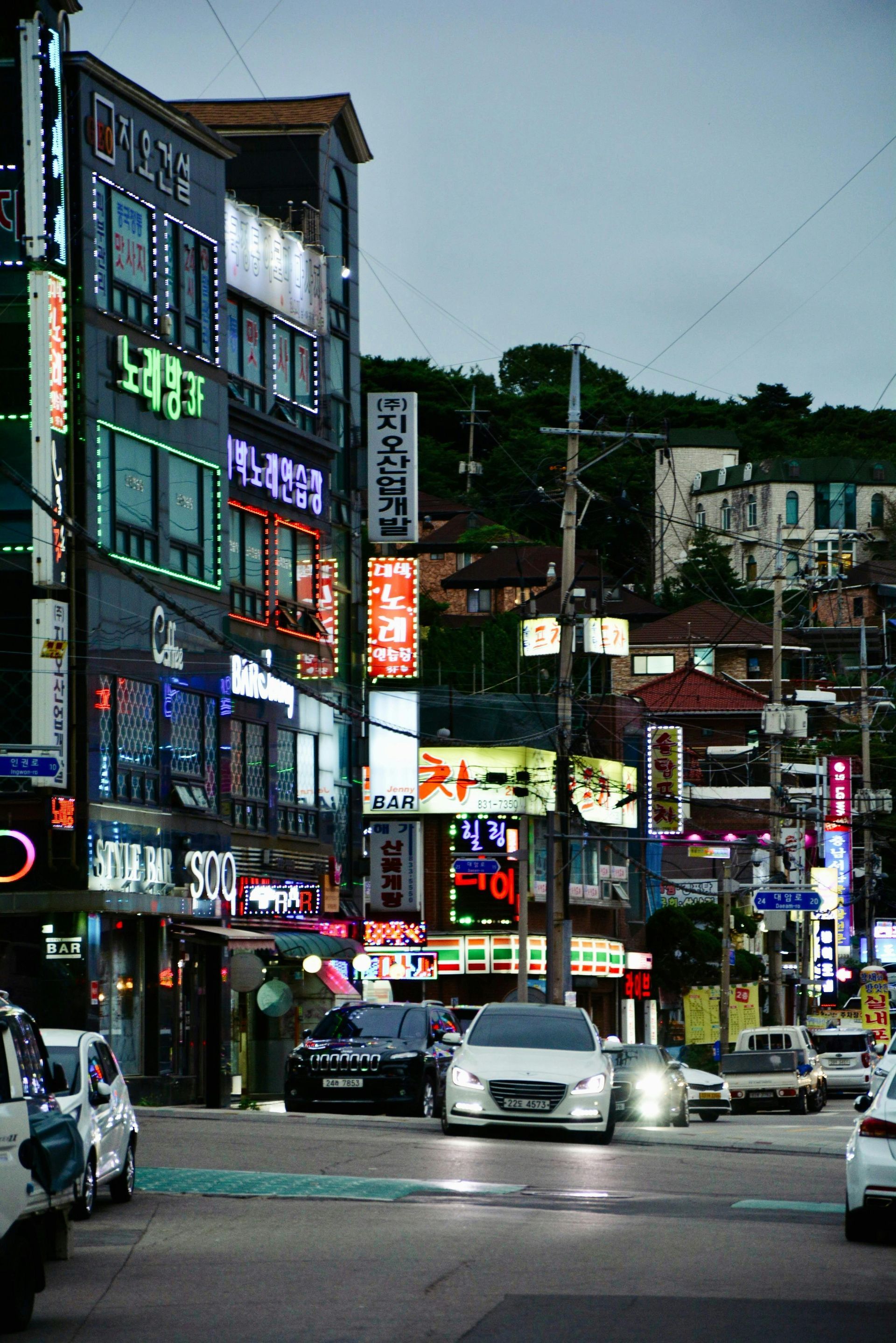 Busy city street at dusk with neon signs, cars, and storefronts lining the road