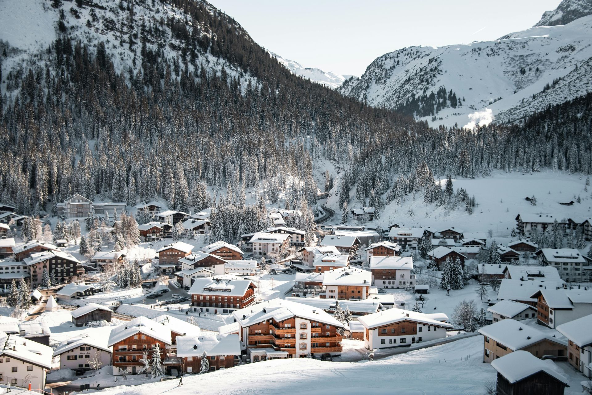 Snow-covered village nestled in a mountain valley, surrounded by snow-dusted trees. Lech am Arlberg