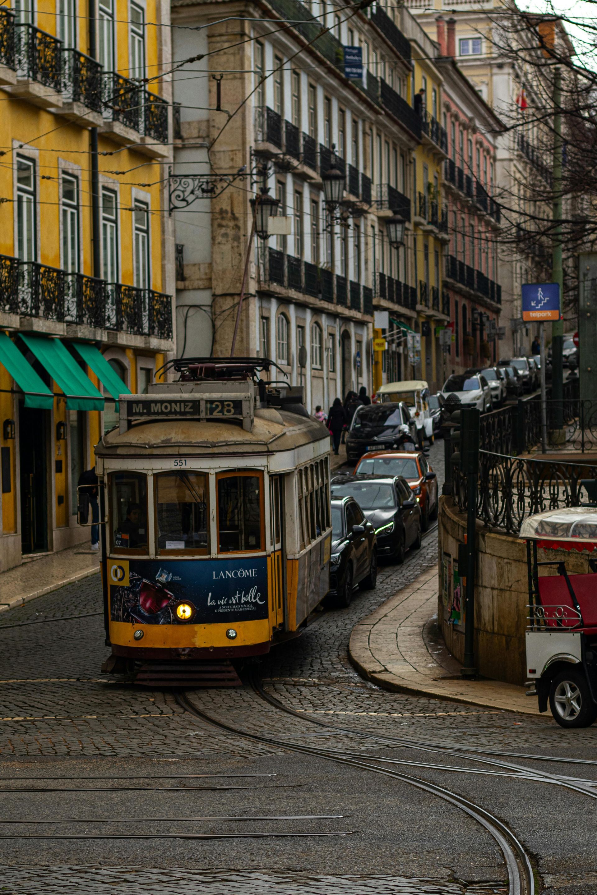 Yellow tram on a steep cobblestone street lined with historic buildings and parked cars.