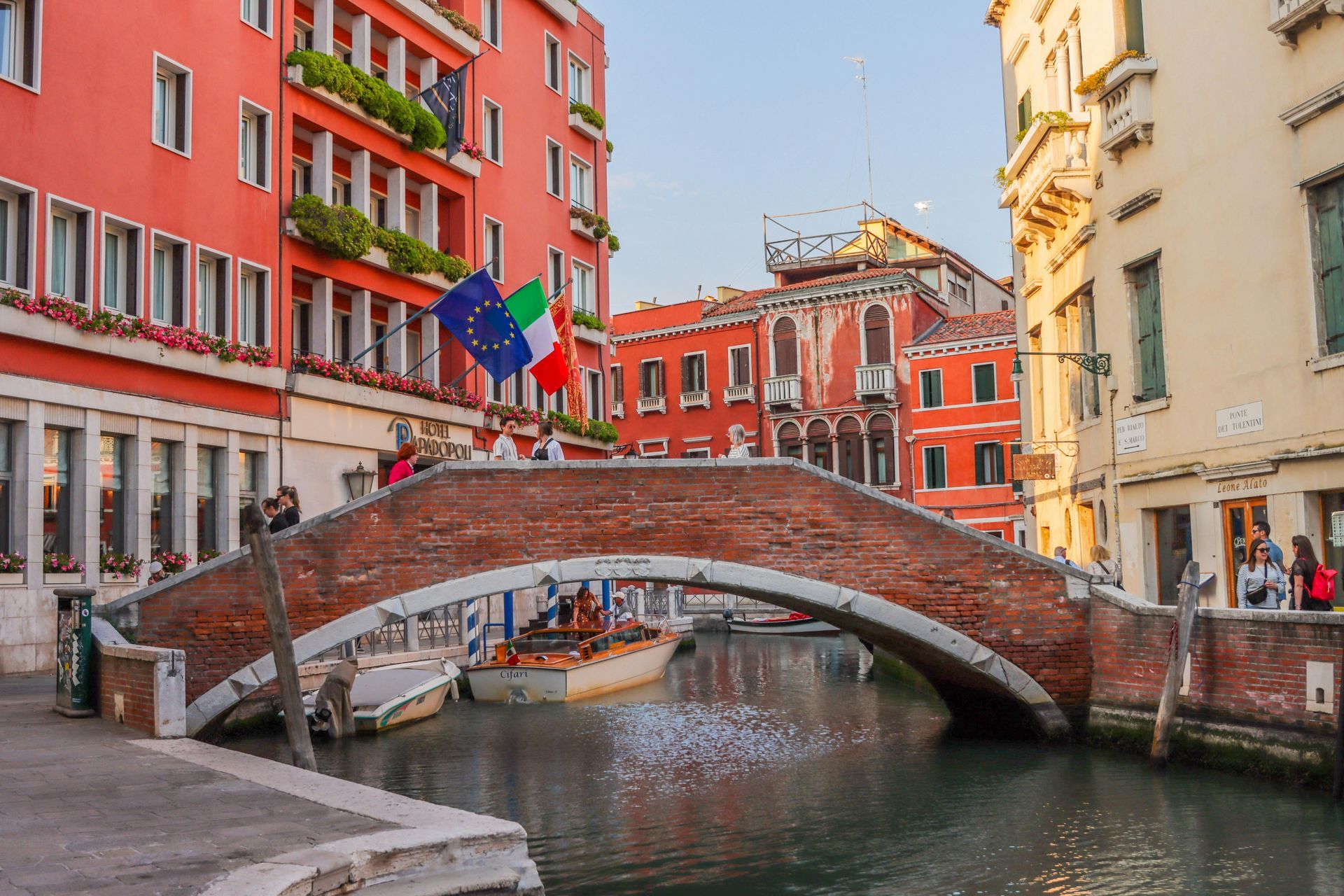 Rialto Bridge in Venice arches over a canal, with a boat docked in front. People walk along the bridge.