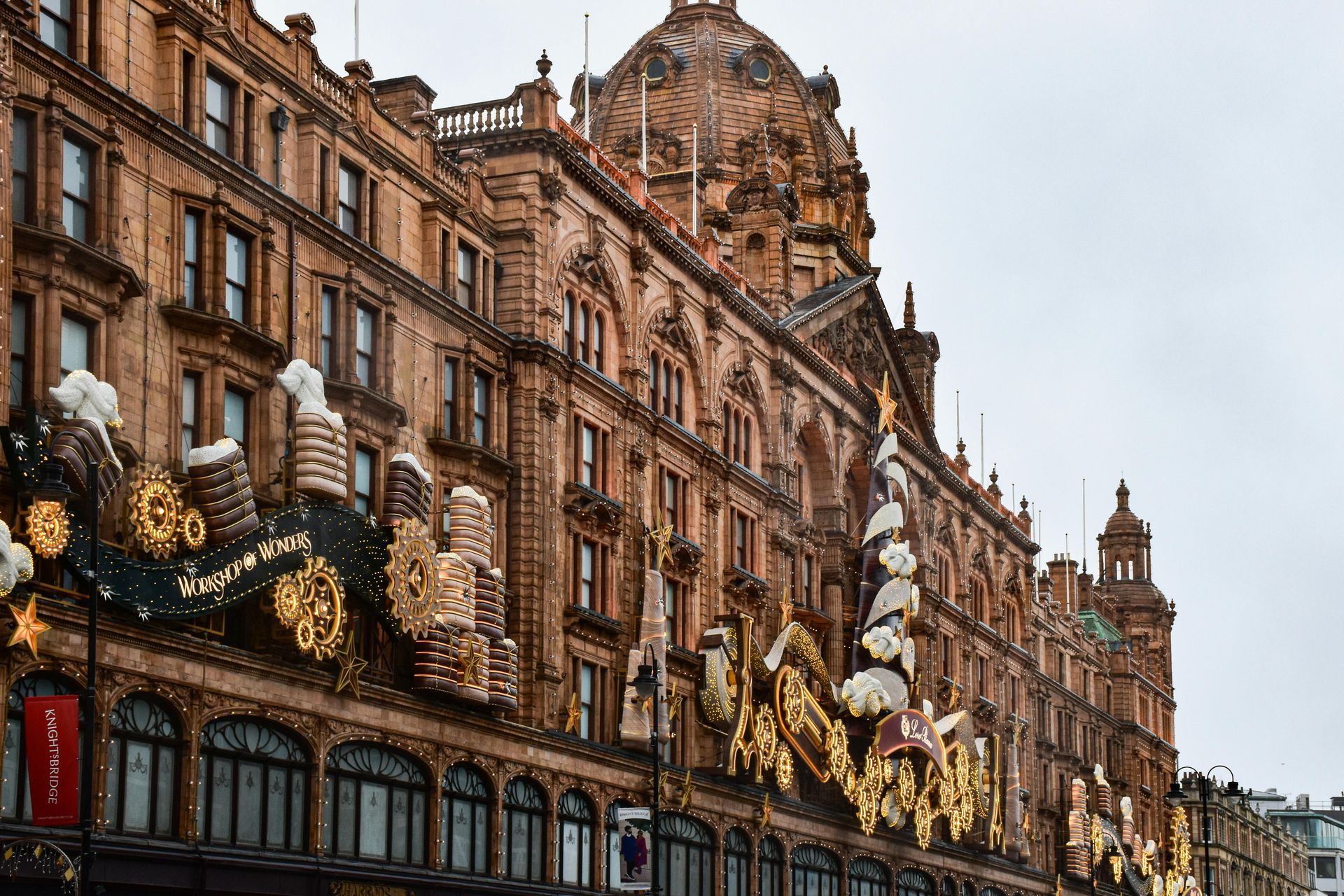 Harrods department store exterior, adorned with Christmas decorations; ornate brown facade, overcast sky.