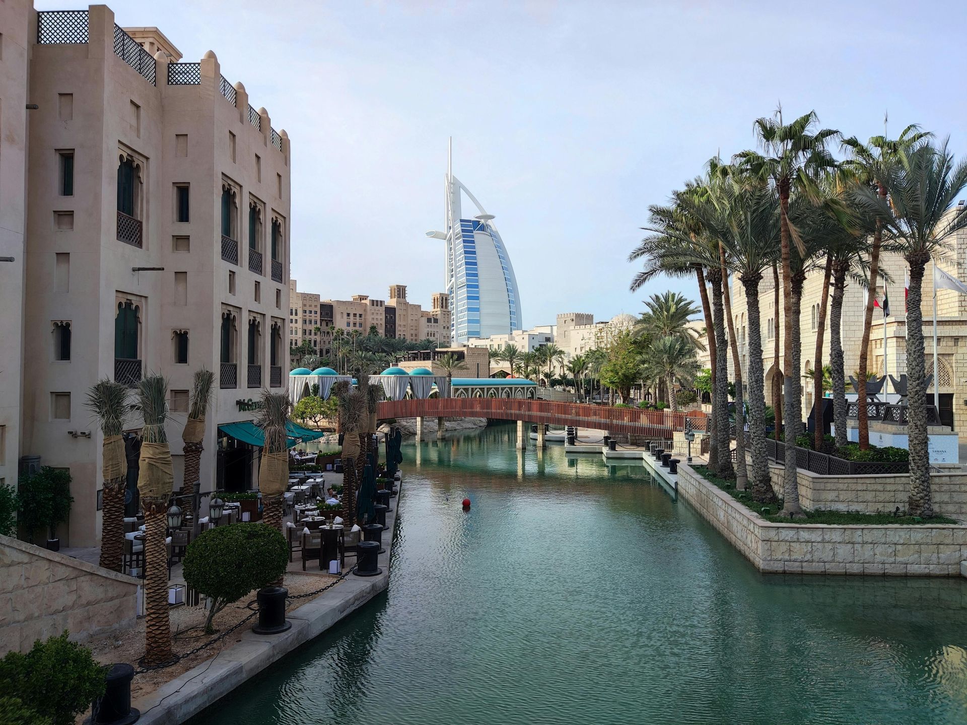 Water canal in Dubai with palm trees, buildings, and Burj Al Arab hotel in the background.