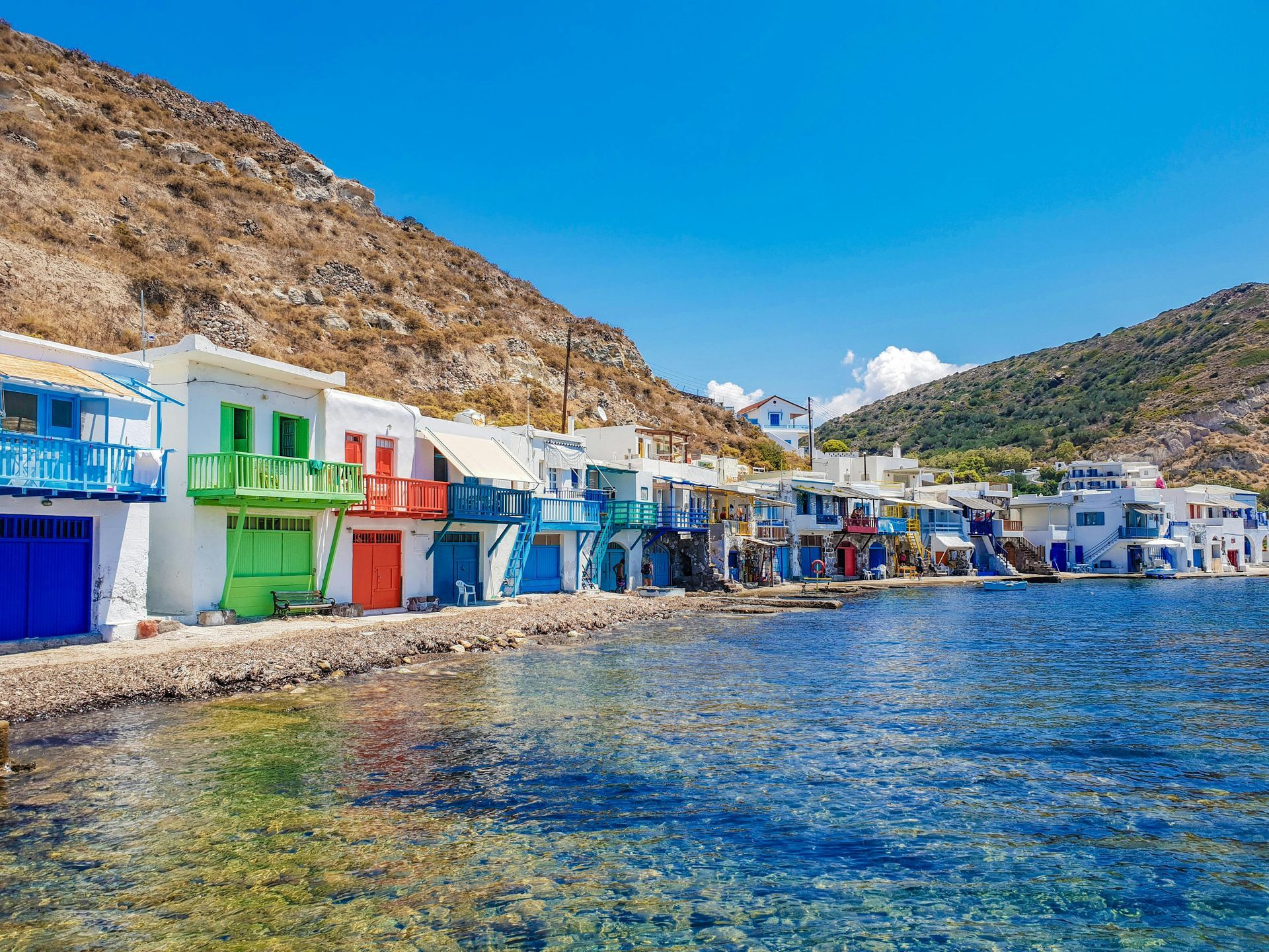 Colorful fishing village on a blue sea under a clear sky, set against a rocky hillside.