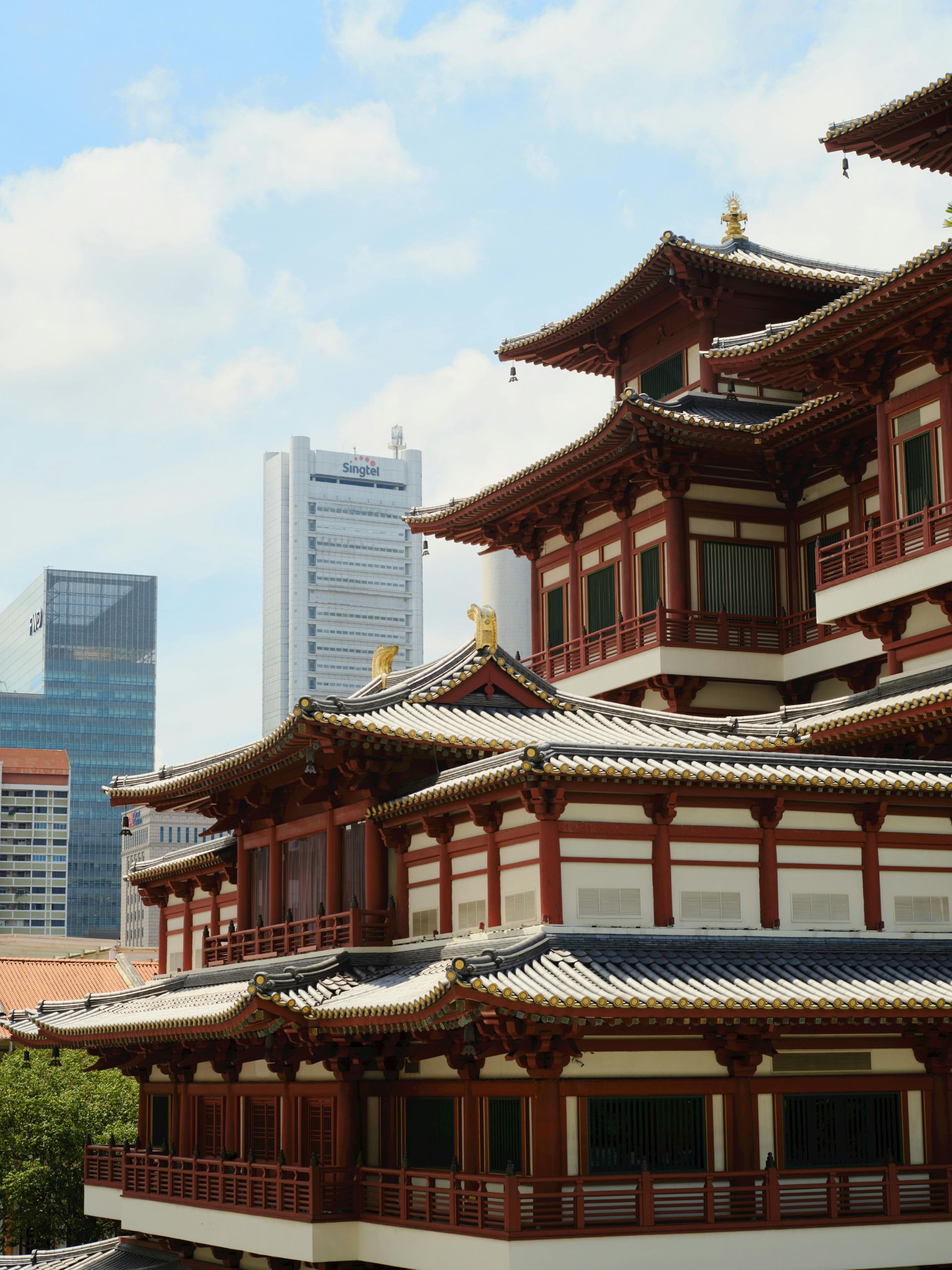 A traditional Chinese-style temple with multi-tiered red and white tiled roofs, set against modern city skyscrapers.