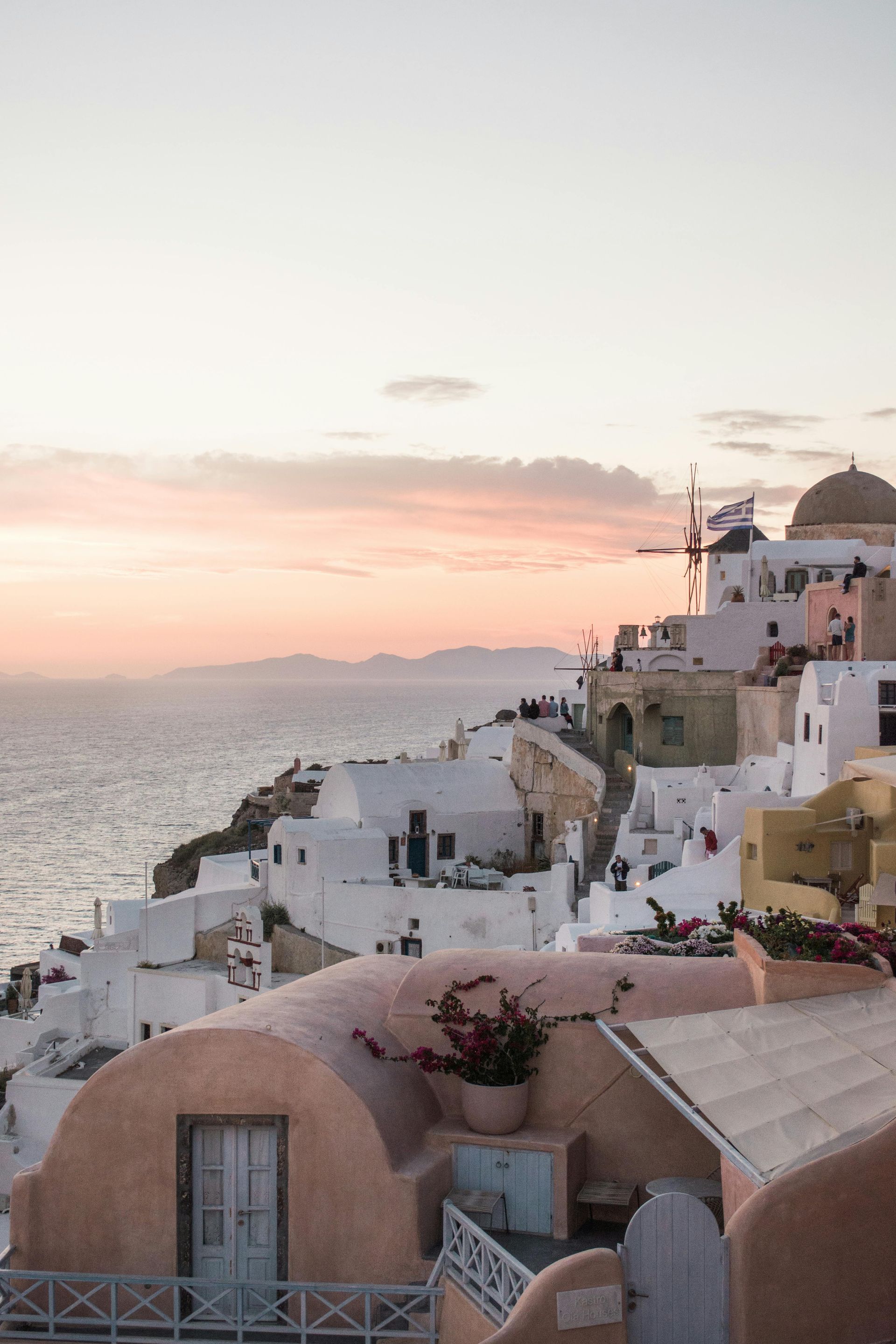 White buildings on a cliff overlooking the sea, bathed in a pink and orange sunset.