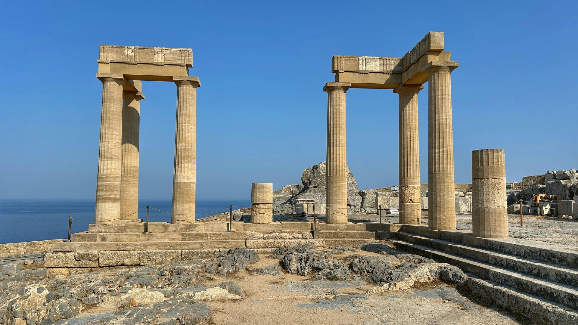 Ruins of ancient columns and structures on a rocky coast under a blue sky. Rhodes
