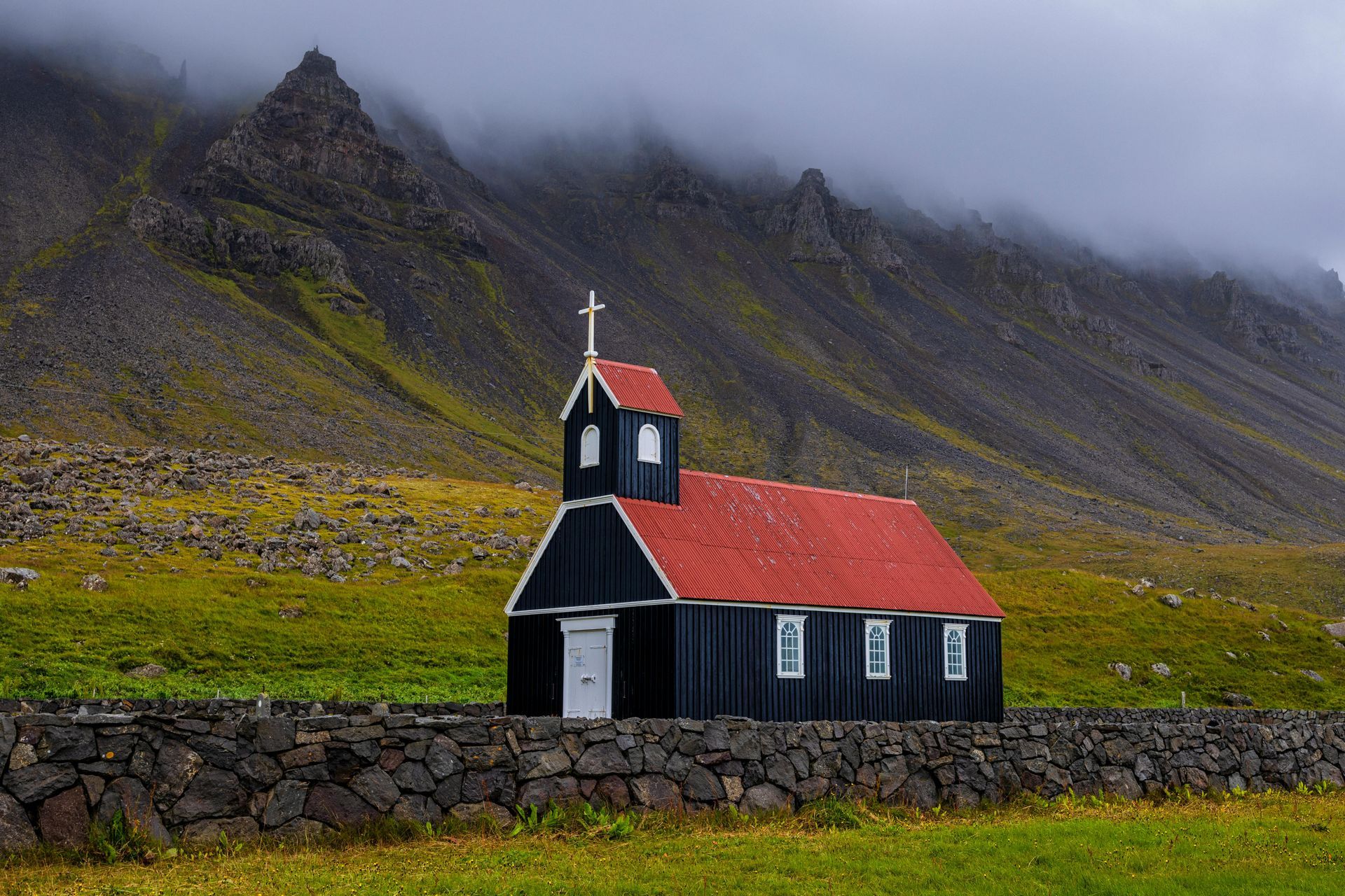 Black church with red roof against a backdrop of mountains and a cloudy sky. Snæfellsnes Peninsula