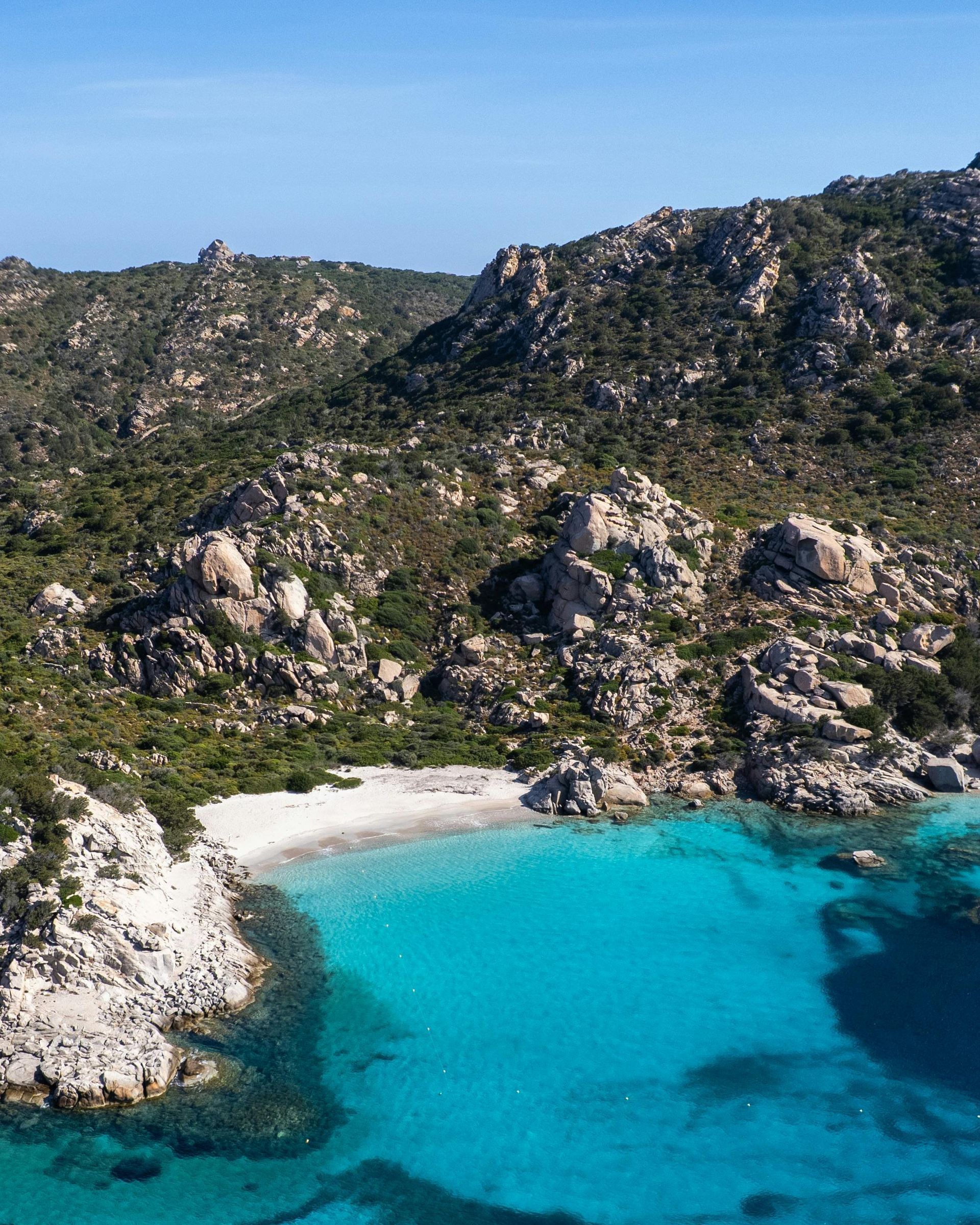 Turquoise cove beside a rocky, green hillside under a clear blue sky