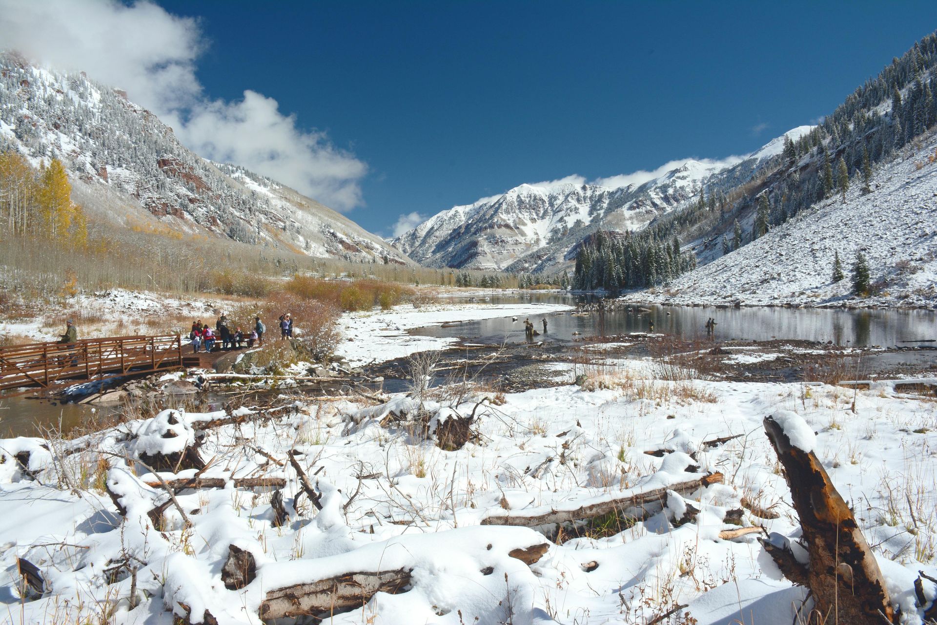 Snowy mountain valley with river and trees, blue sky.