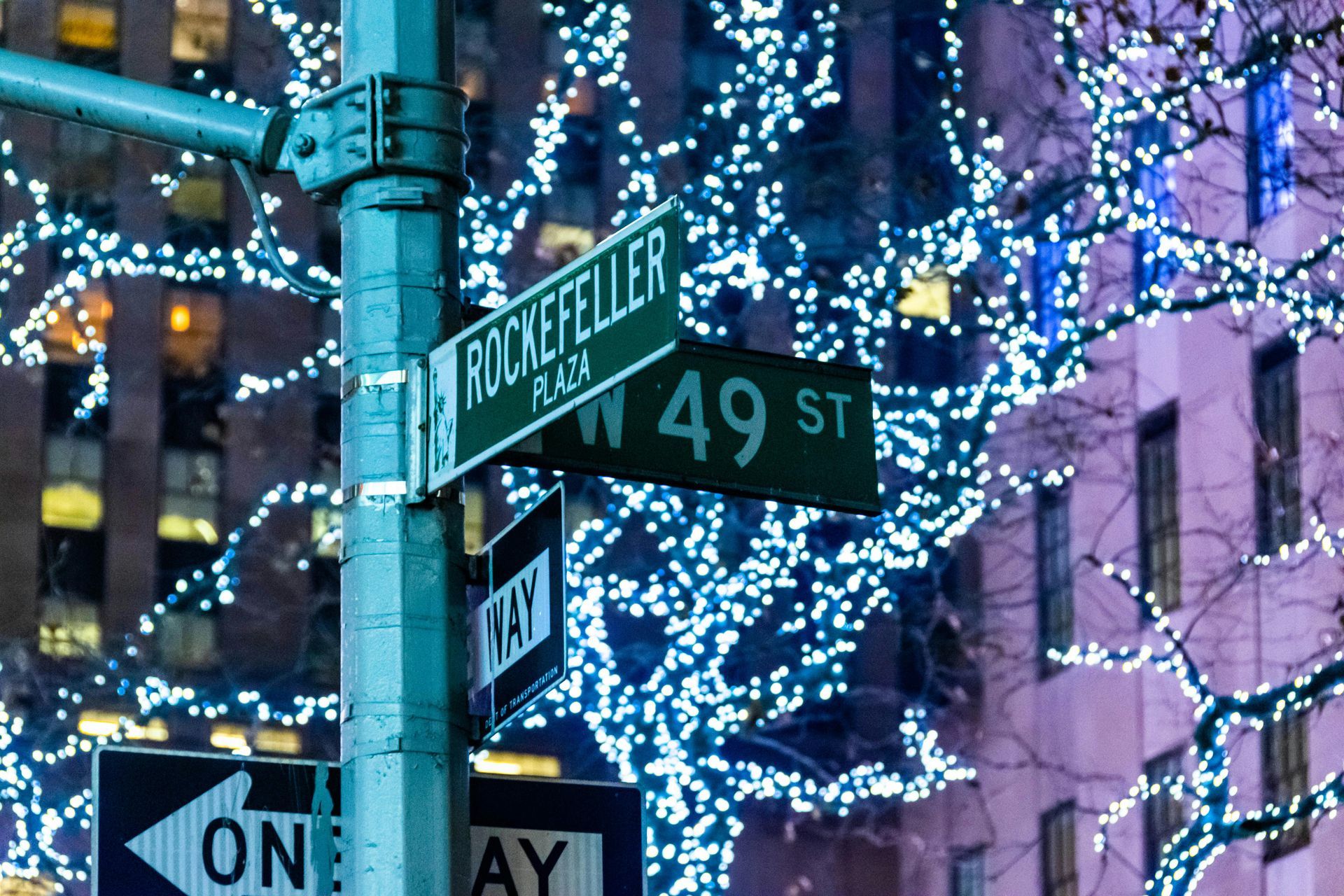 Rockefeller Plaza street sign, illuminated by holiday lights in New York City.