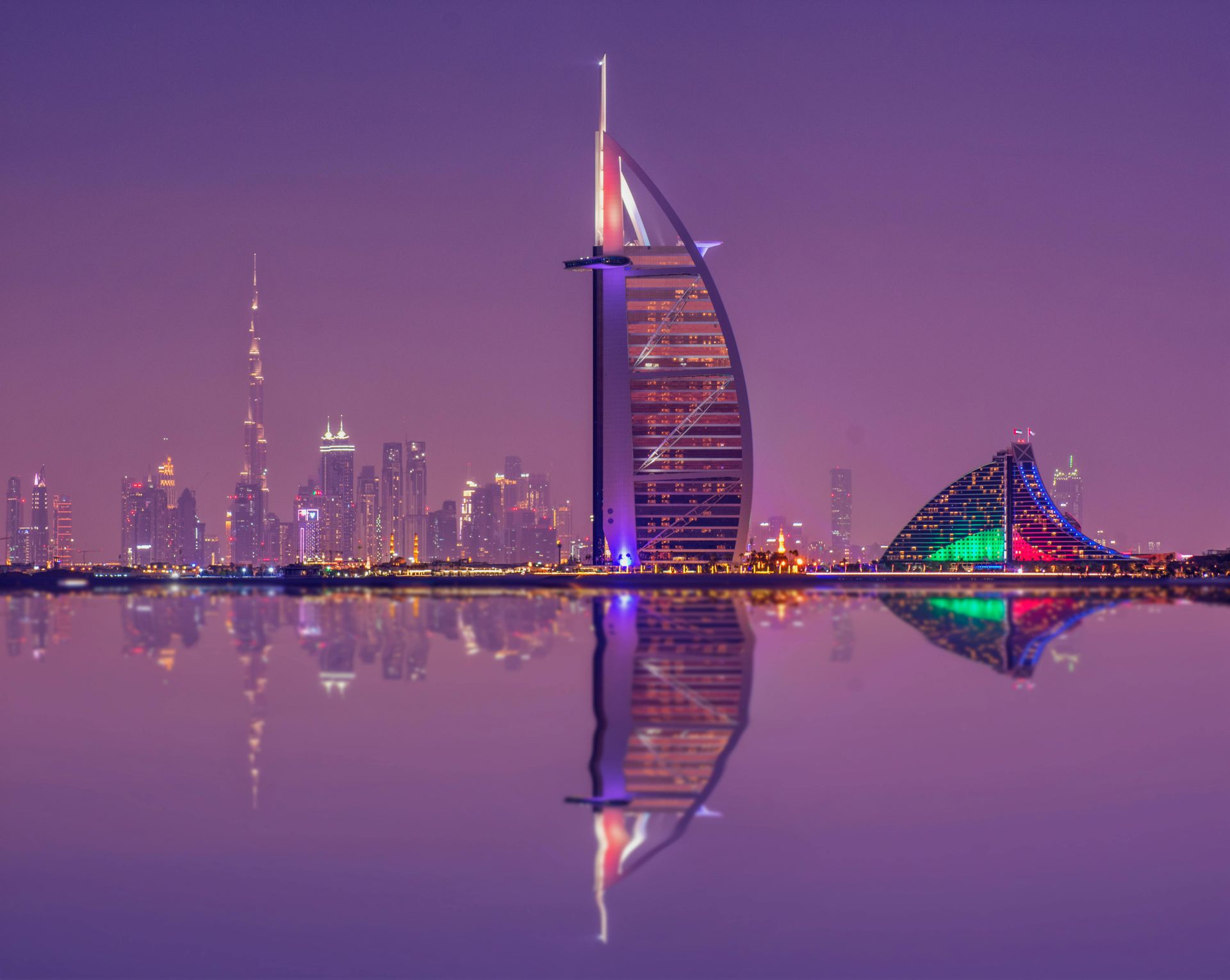 Dubai skyline at dusk, with Burj Al Arab hotel reflected in calm water. Purple hues, city lights.