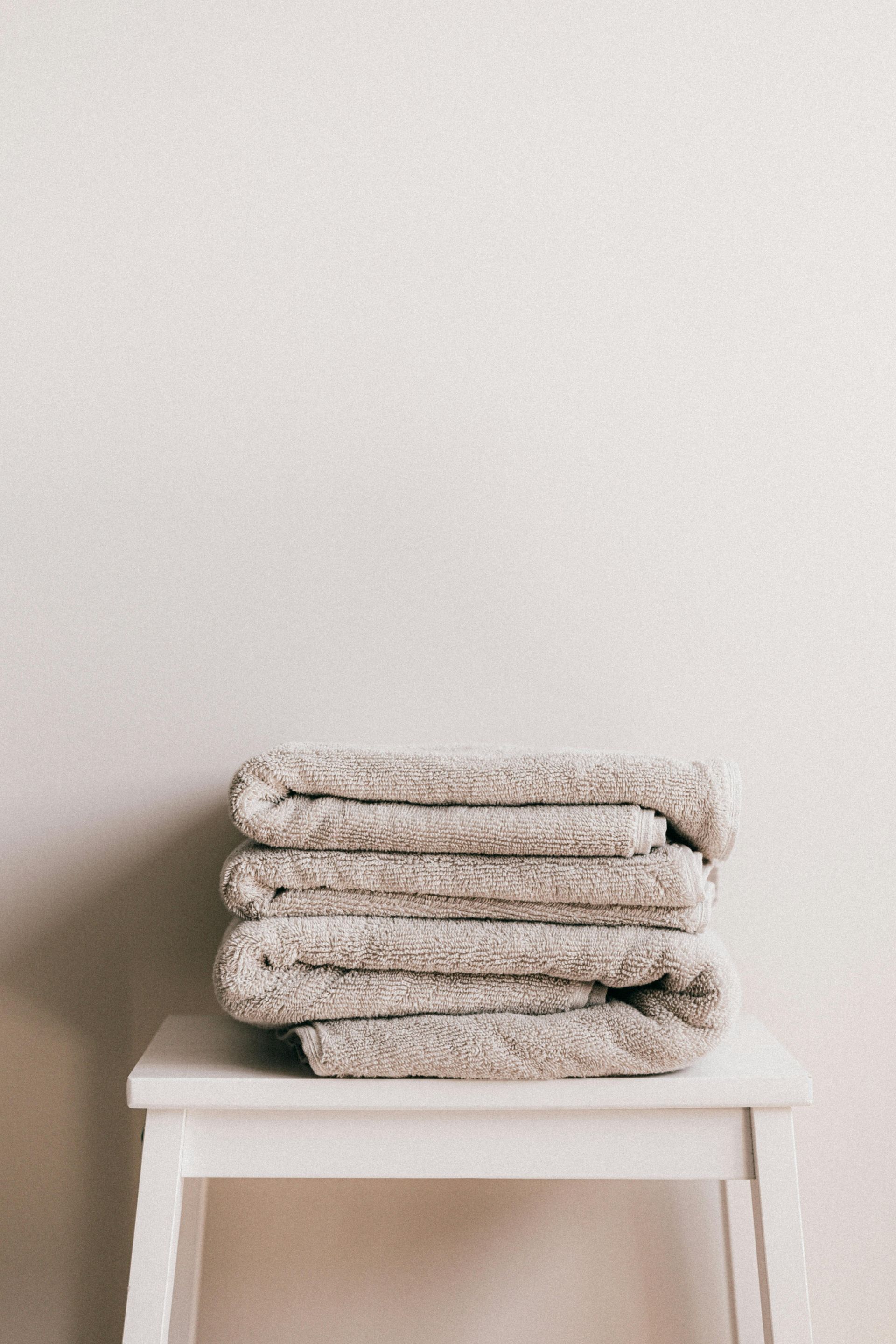 Stack of folded gray towels on a white stool against a white wall.