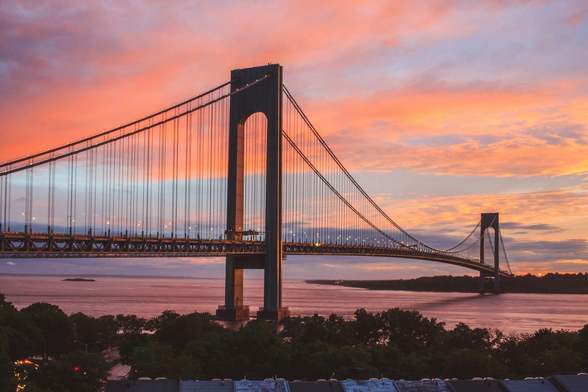 Verrazano-Narrows Bridge silhouetted against a vibrant sunset sky over the water.
