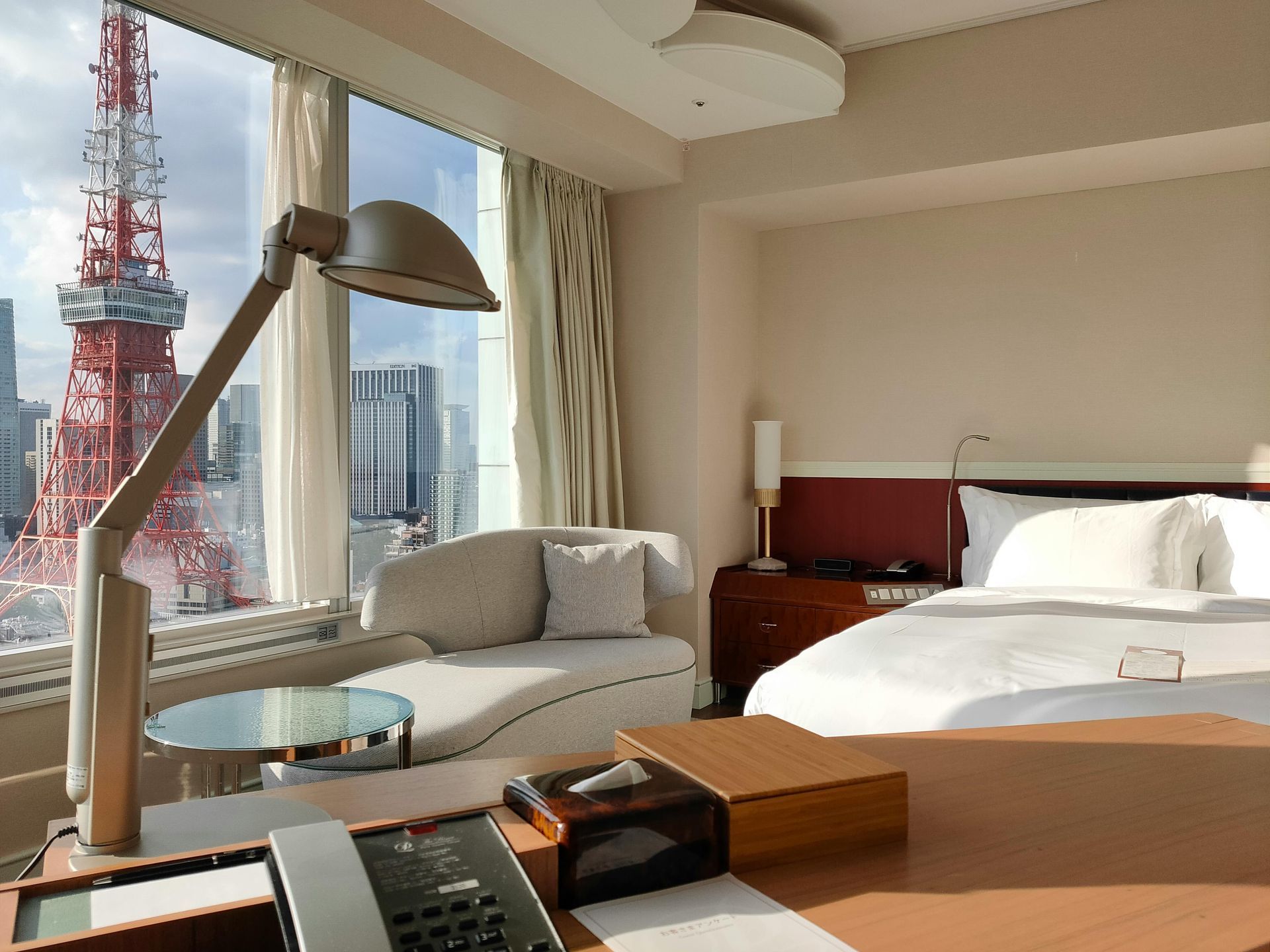 Hotel room with Tokyo Tower view, desk with lamp, bed, and small sofa.